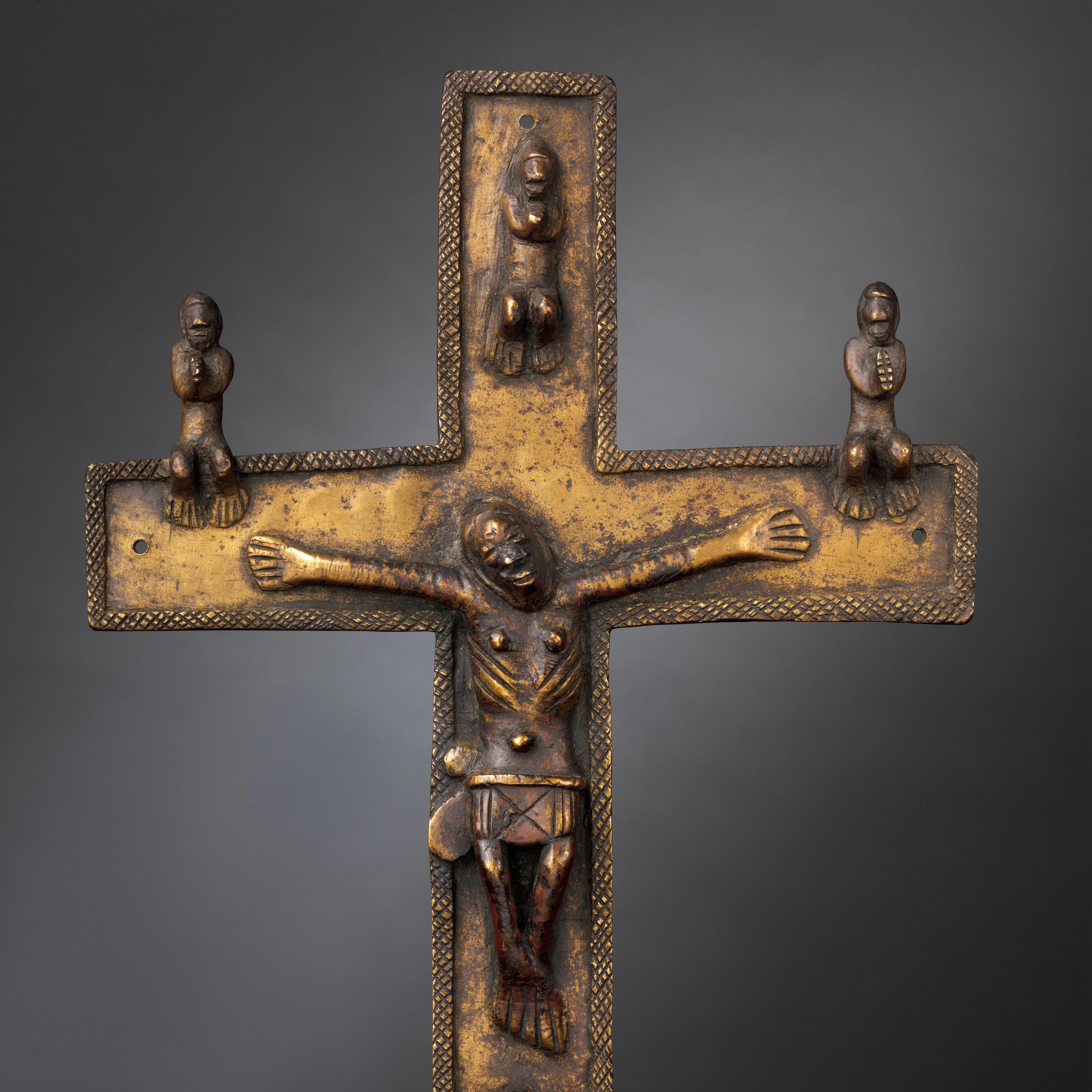 A brass cast crucifix featuring a Christ figure cast in relief, arms extended, with three smaller figures on the apex and arms of the cross.
