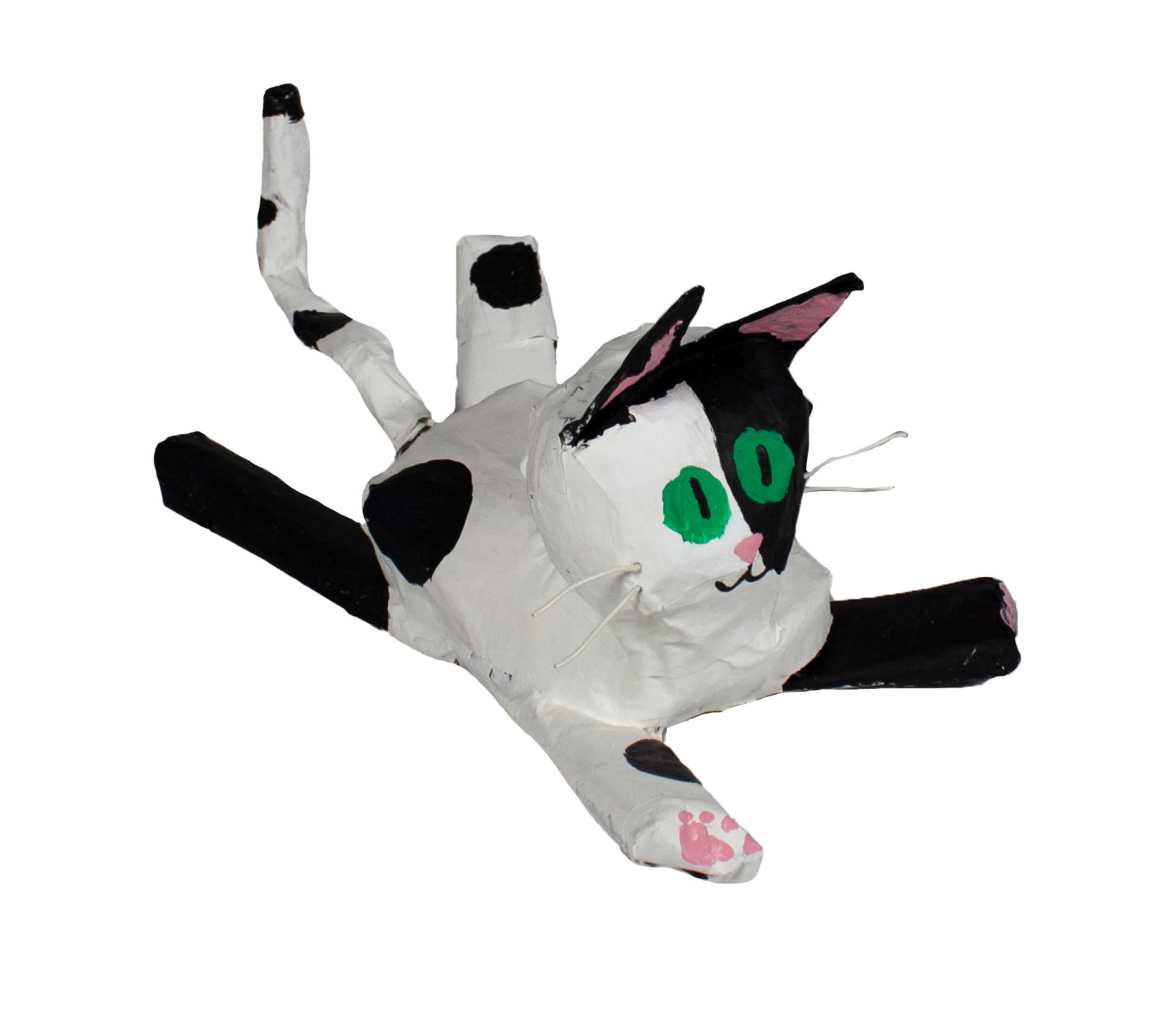 Papier mâché sculpture of white cat with round green eyes and black spots, lying splayed on all four extended legs, facing rightward, with a wry smile on its face. The cat's pink paws, pink nose, and pink inner ears are visible. The cat's left front leg, right rear leg, and left side of its face are black. Two white whiskers extend from the right side of the cats' face, and two darker whiskers extend from the left.