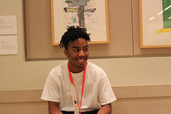 A young man with short locks wearing a white t-shirt sitting in front of a kid's painting