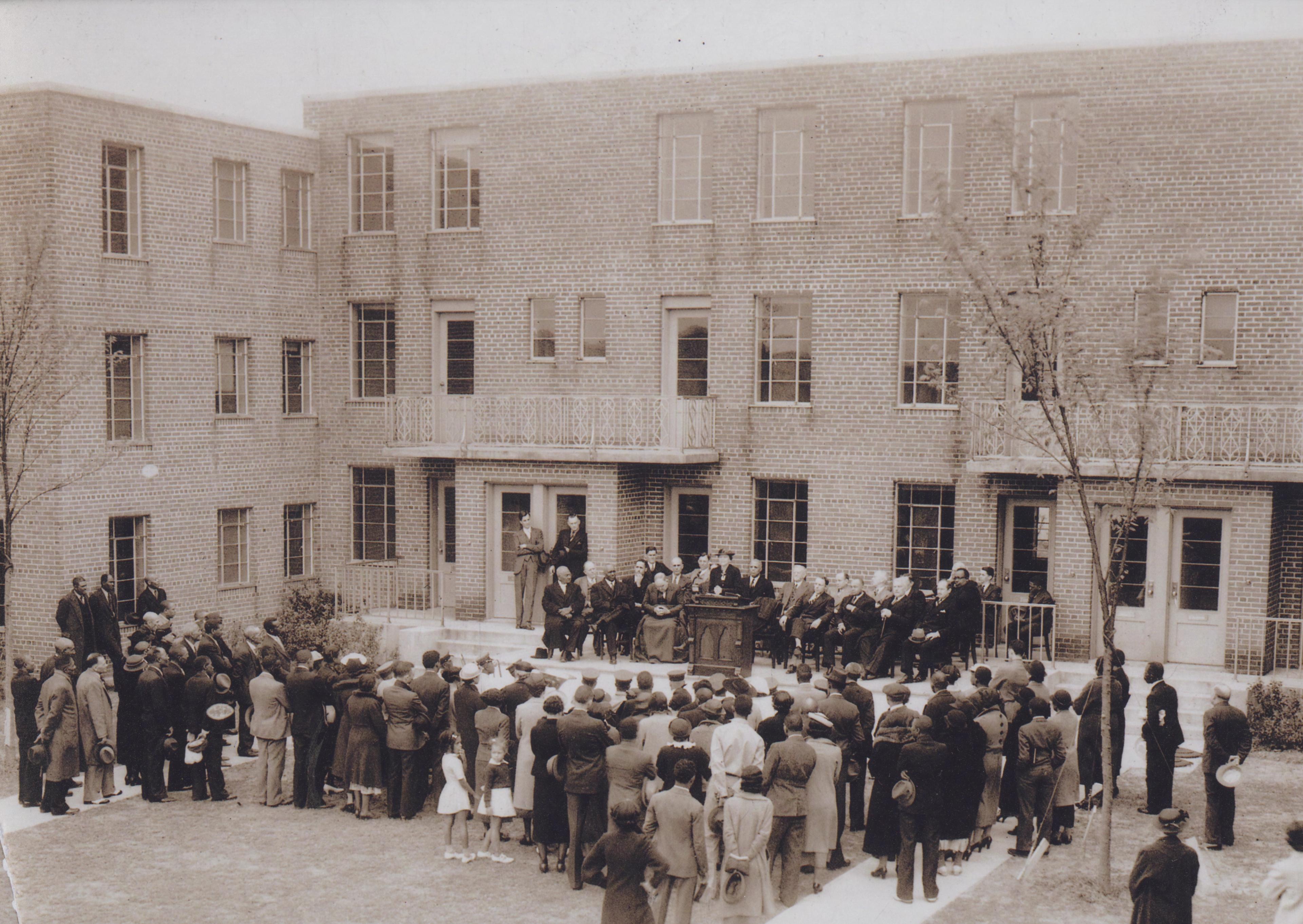 Photograph of a group of people gathered at the dedication ceremony for University Homes. 