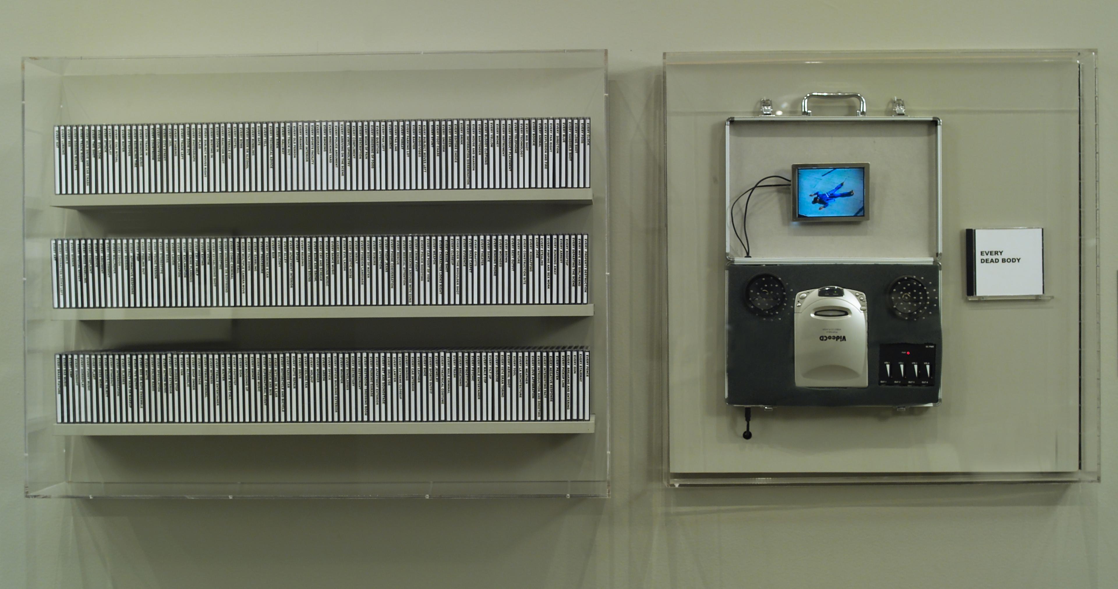 At left, three wall-mounted shelves of CDs. To the right of the shelves, a video CD player with exposed wires, attaching to a small screen showing a figure in blue lying face down. To the right of the player is a small CD with cover art that reads "EVERY DEAD BODY." 