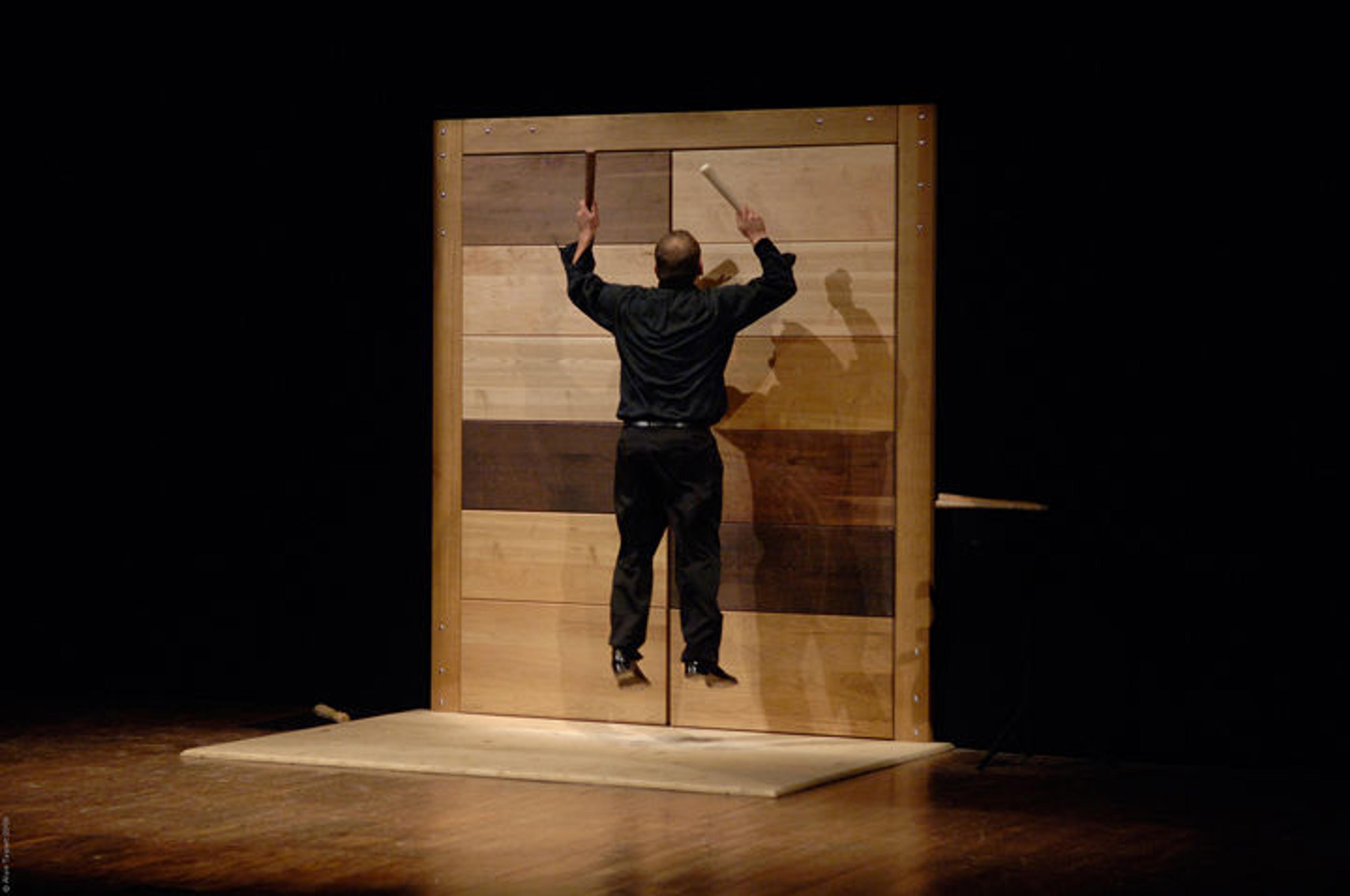 A percussionist jumps into the air to strike a large metal door with two hammers