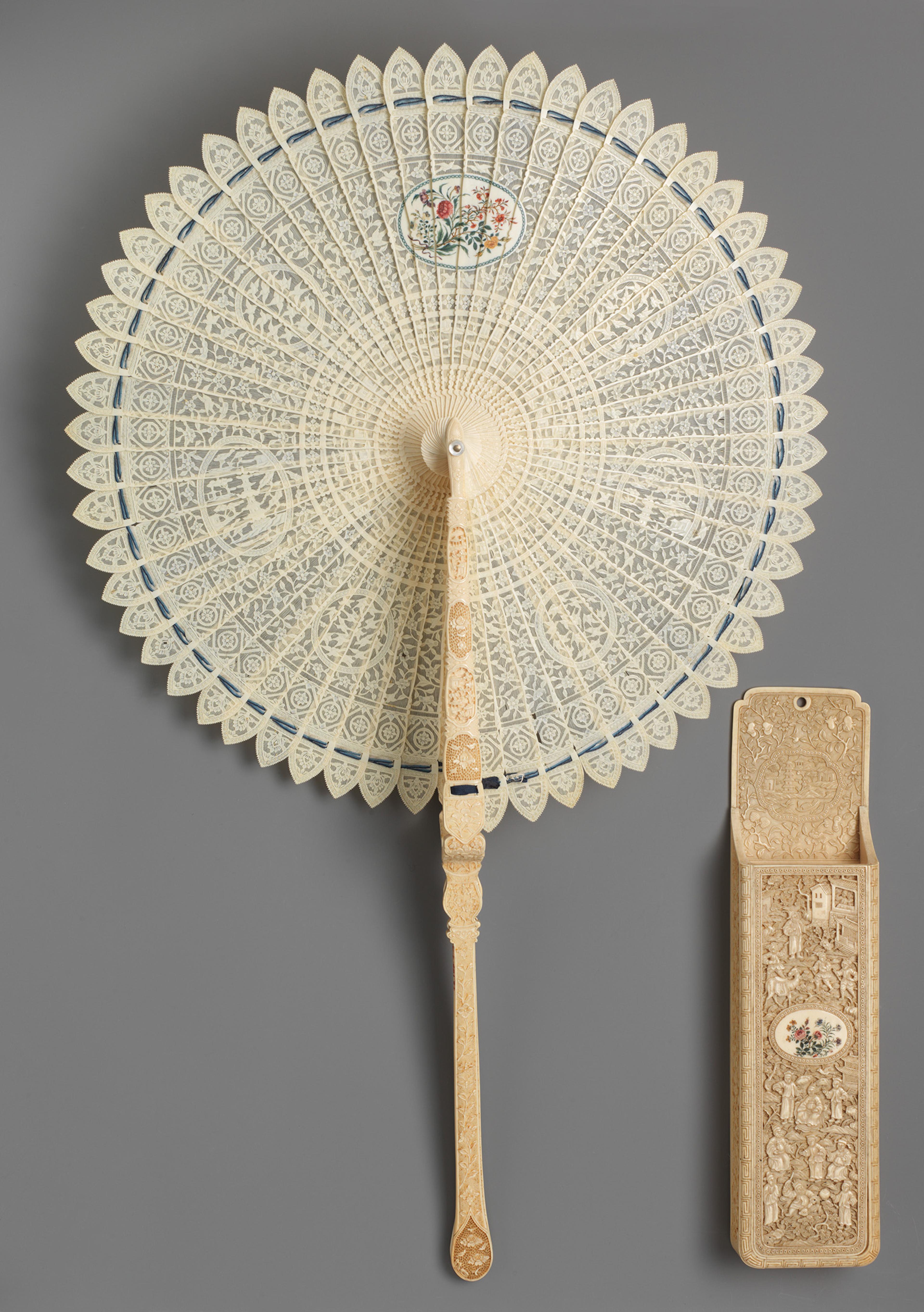 Ornate openwork ivory fan with intricate circular design and floral motif. Accompanied by a matching decorated case.