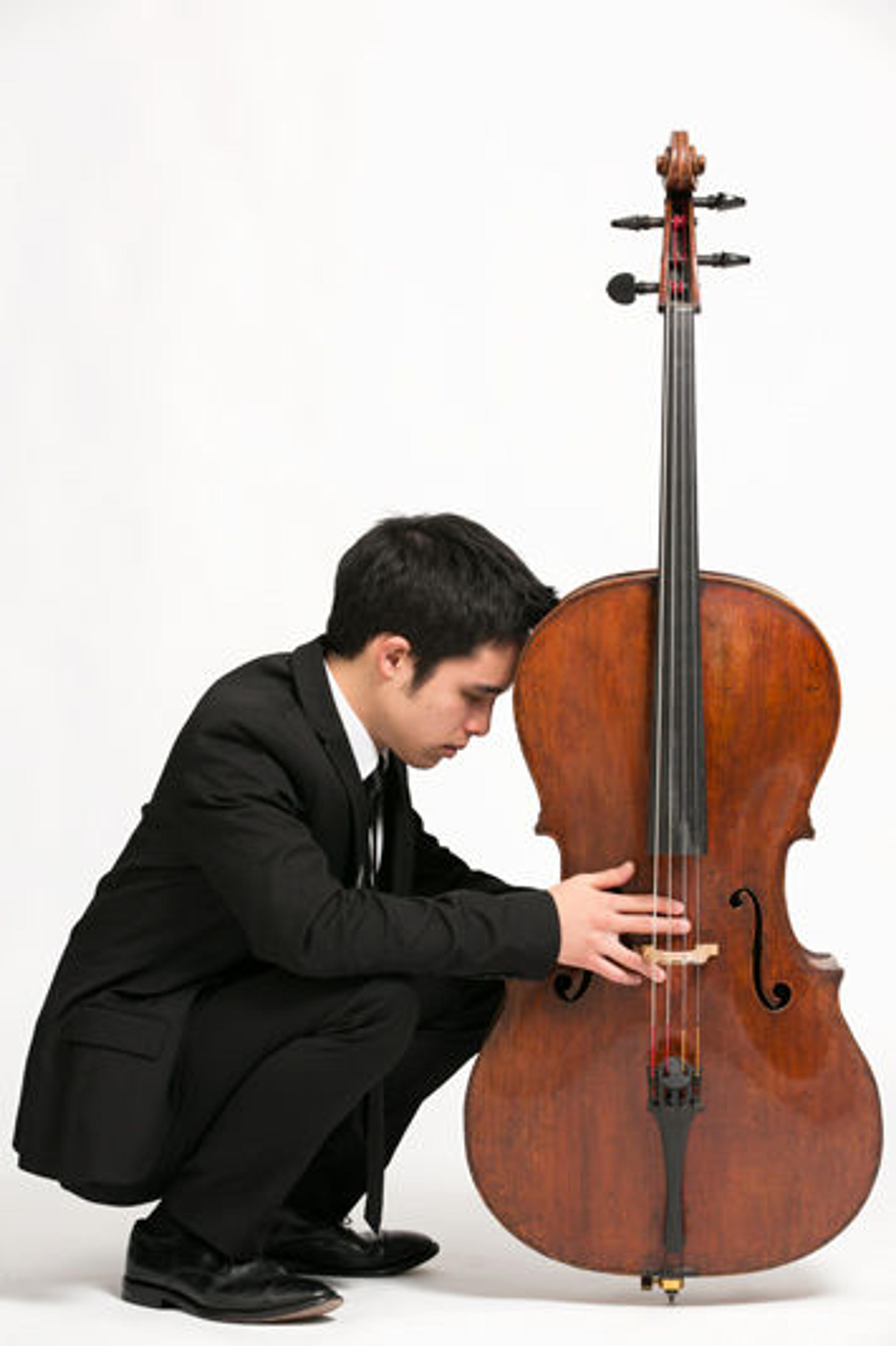 Man squatting, his head pressed to a cello