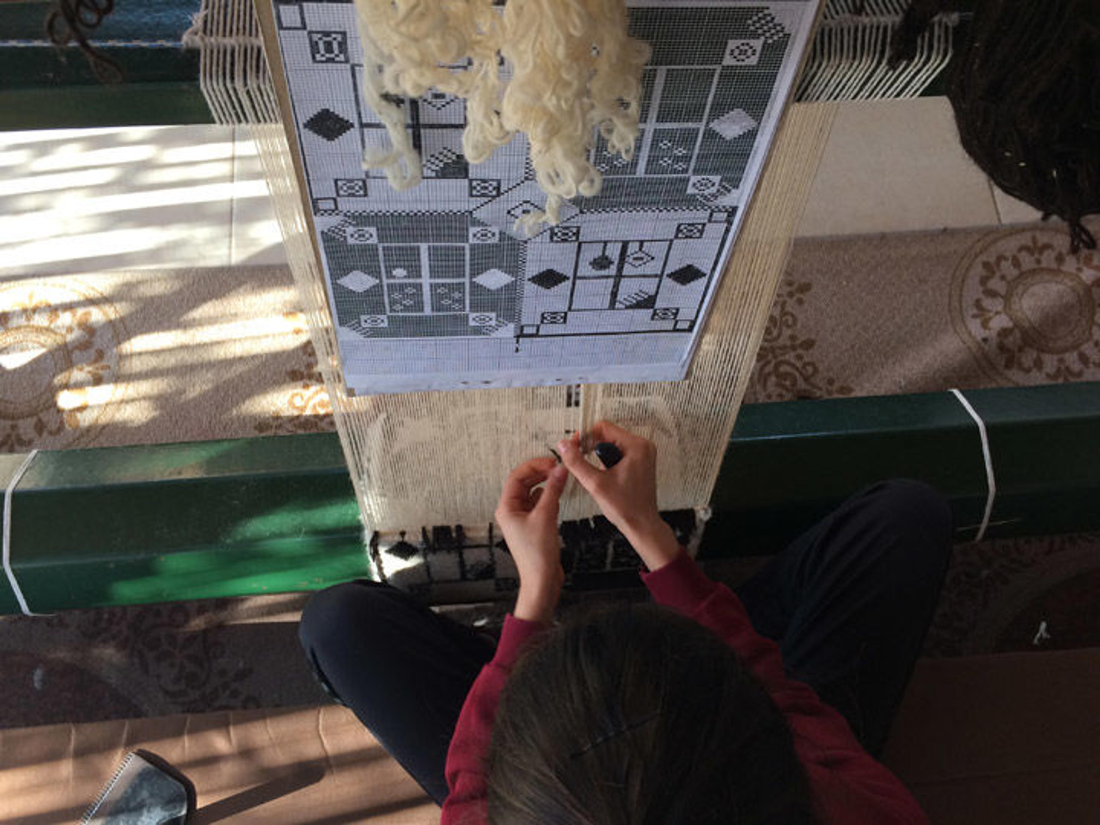 A woman weaver sits at a loom