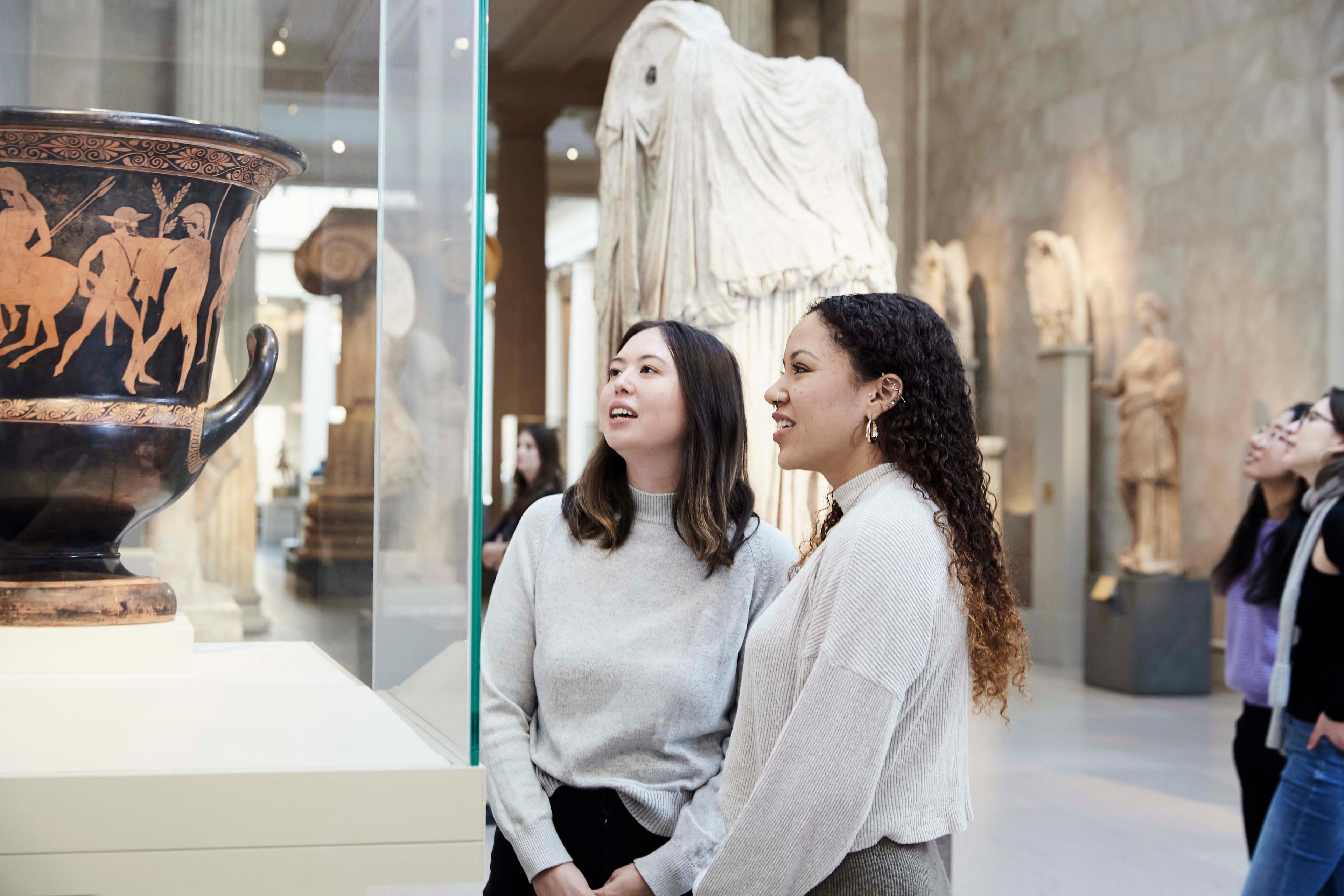 Two young women look at an amphora in the Greek and Roman galleries at The Met.
