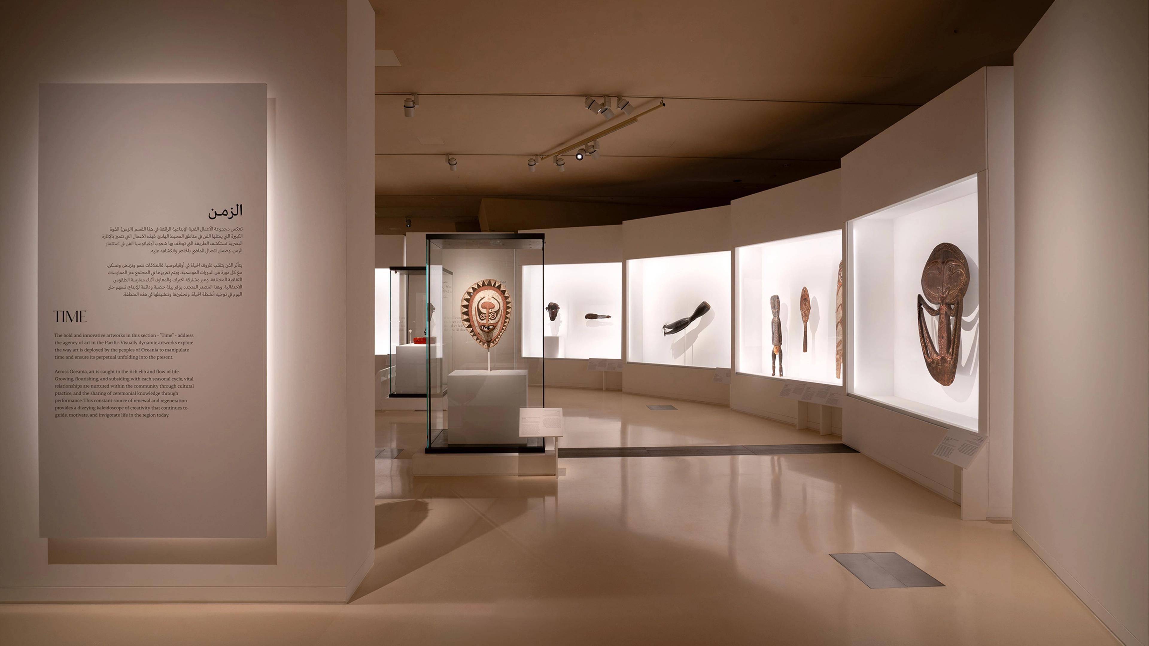 Dimly lite exhibition galleries featuring illuminated display cases with masks and artifacts, alongside descriptive panels.