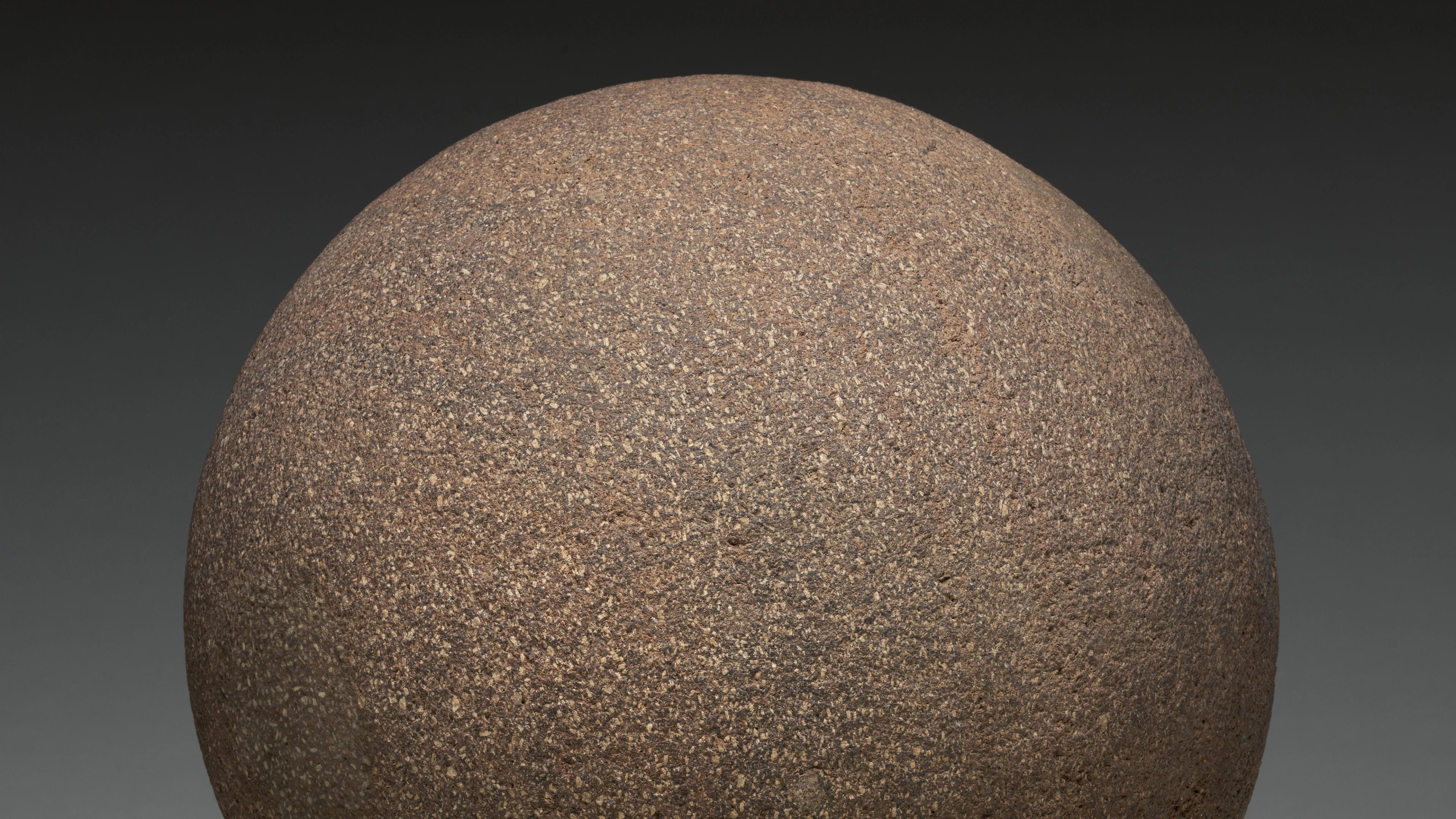 Photograph of a gray-brown stone sphere against a black background