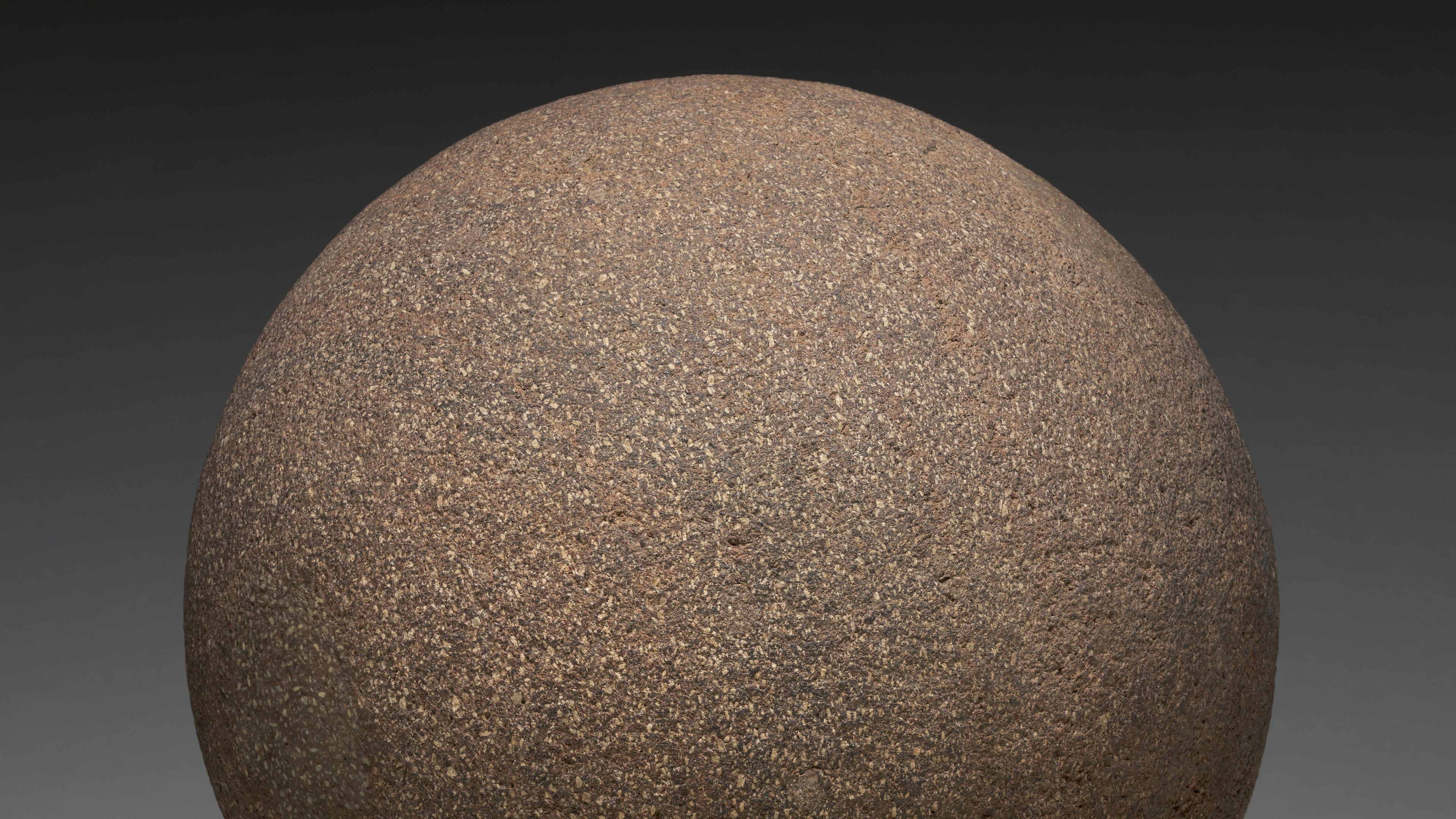 Photograph of a gray-brown stone sphere against a black background