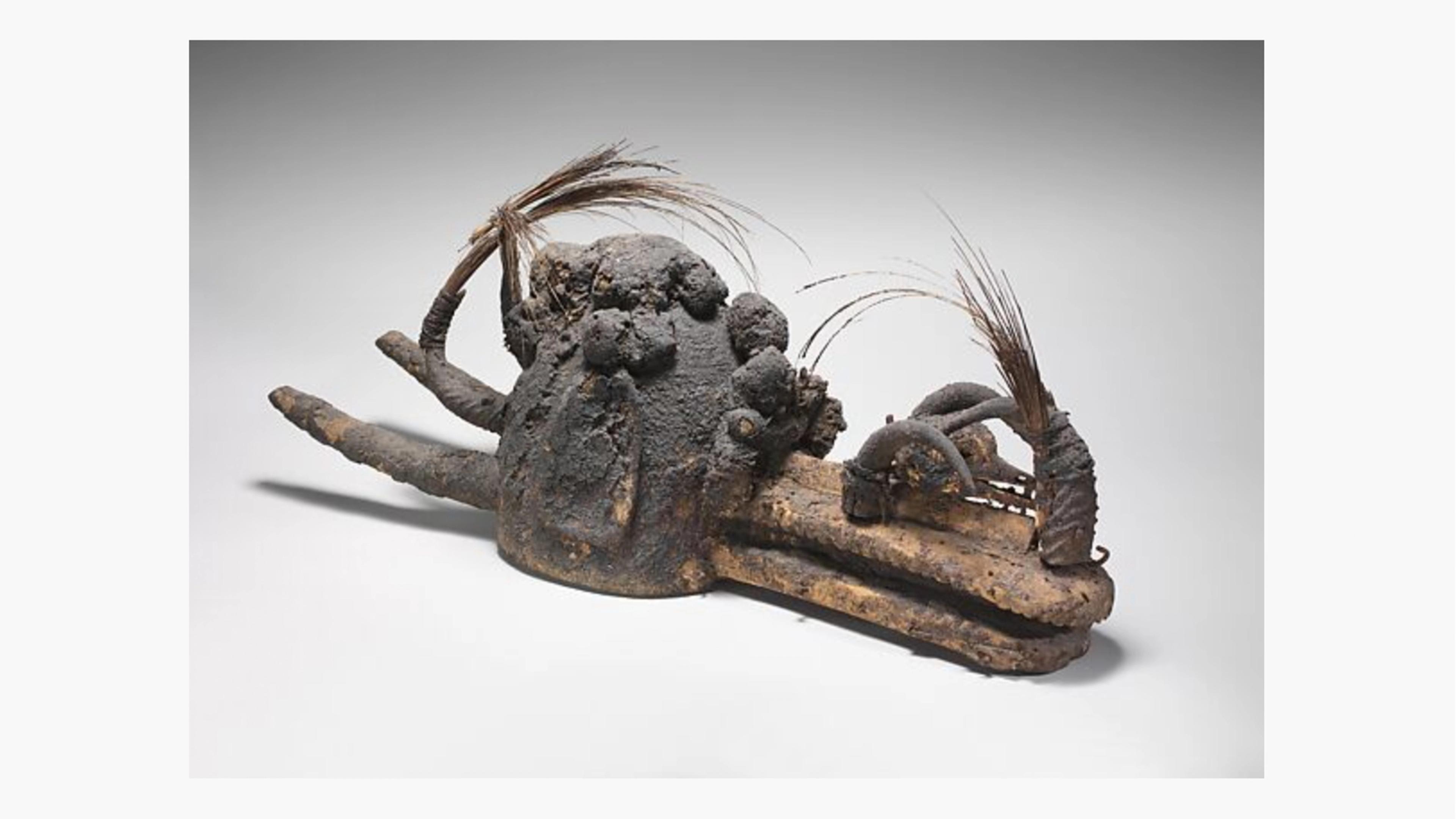 A wooden helmet mask covered with animal horns, a bird skull, porcupine quills, feathers, bundles, and a thick grayish coating