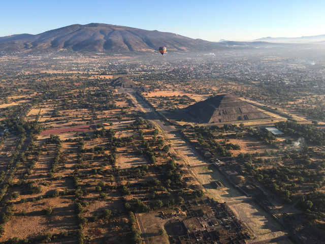 Hot air balloon over landscape with a pyramid and a mountain in the background