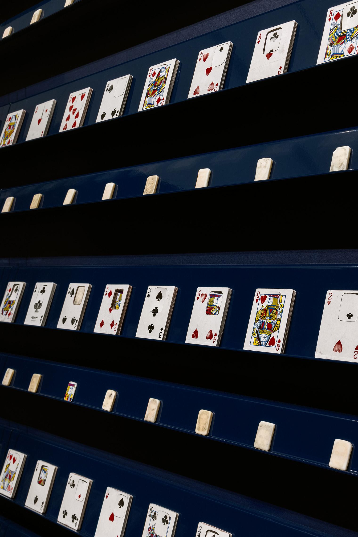 Rows of playing cards displayed on blue shelves, featuring various suits and numbers, creating a playful and organized visual theme.