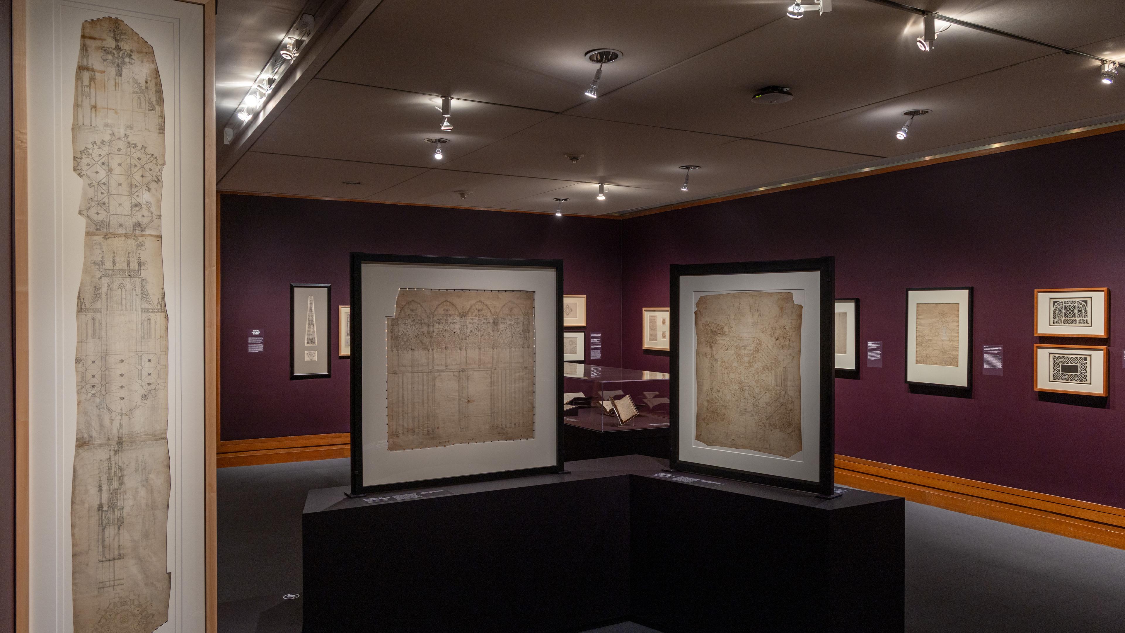 Exhibition room with framed architectural sketches on dark purple walls.