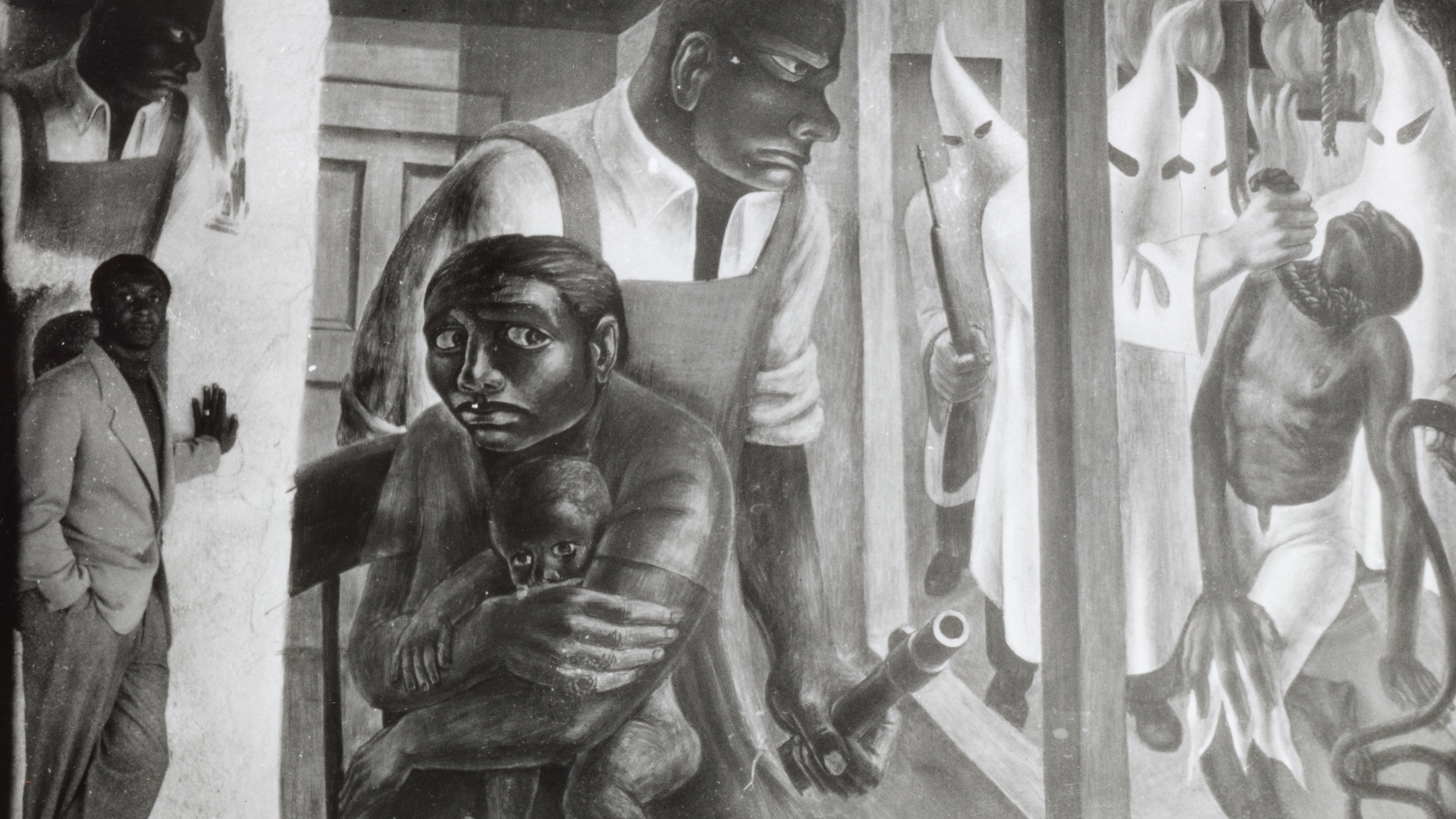Black and white image of man standing next to mural depicted in black and white of a mother shielding her baby and while a strong black meale guards her. 