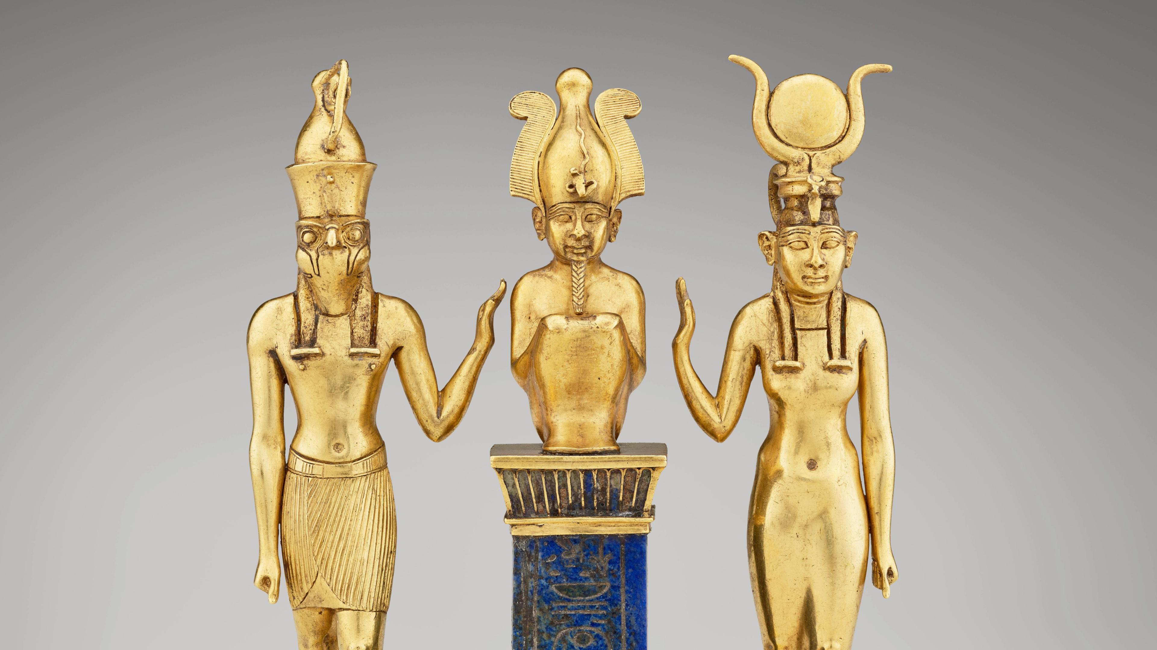 A golden statue of three standing figures with elaborate headdresses