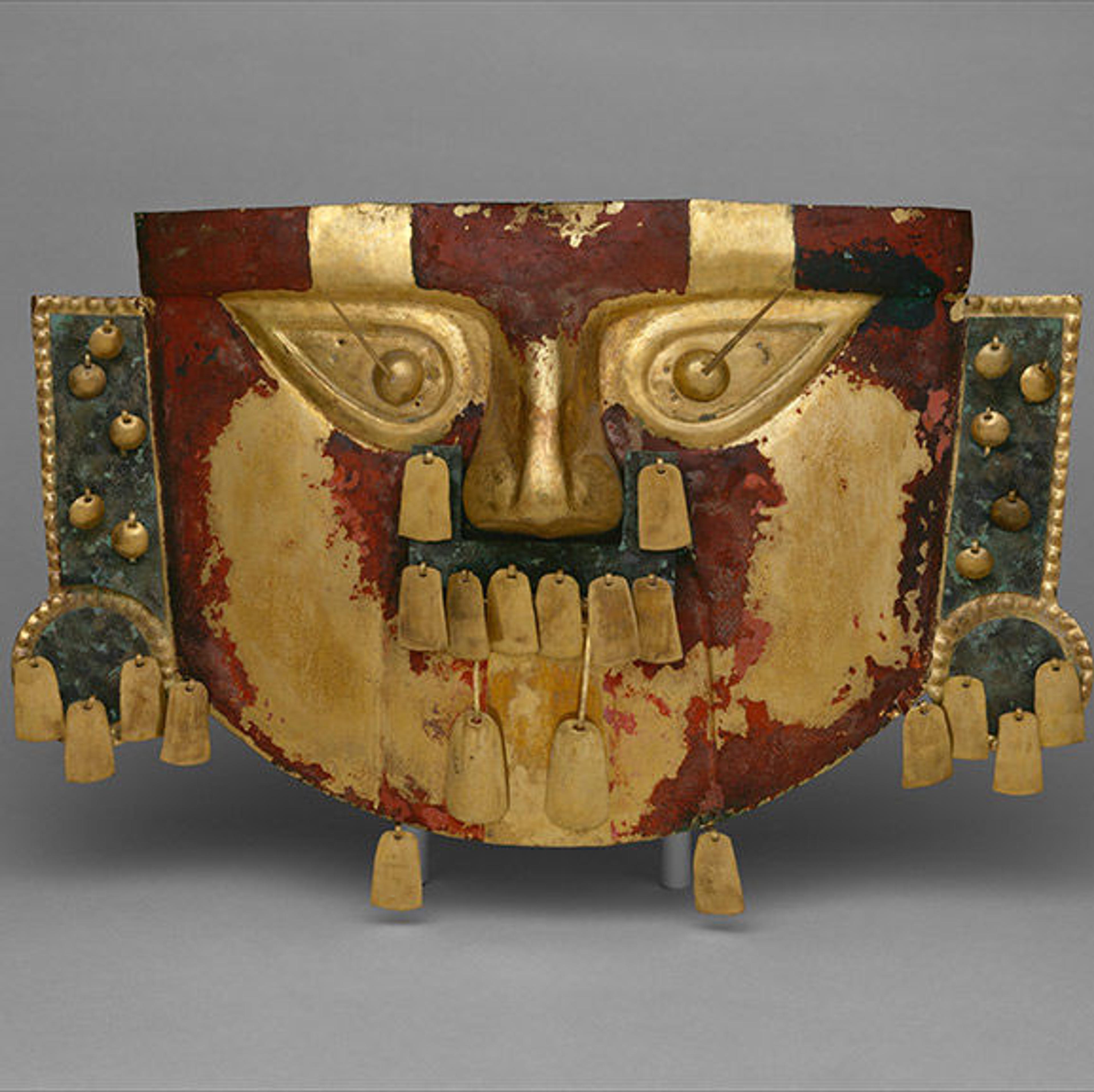 A photograph of a gold, red, and green funerary mask with prominent facial features.