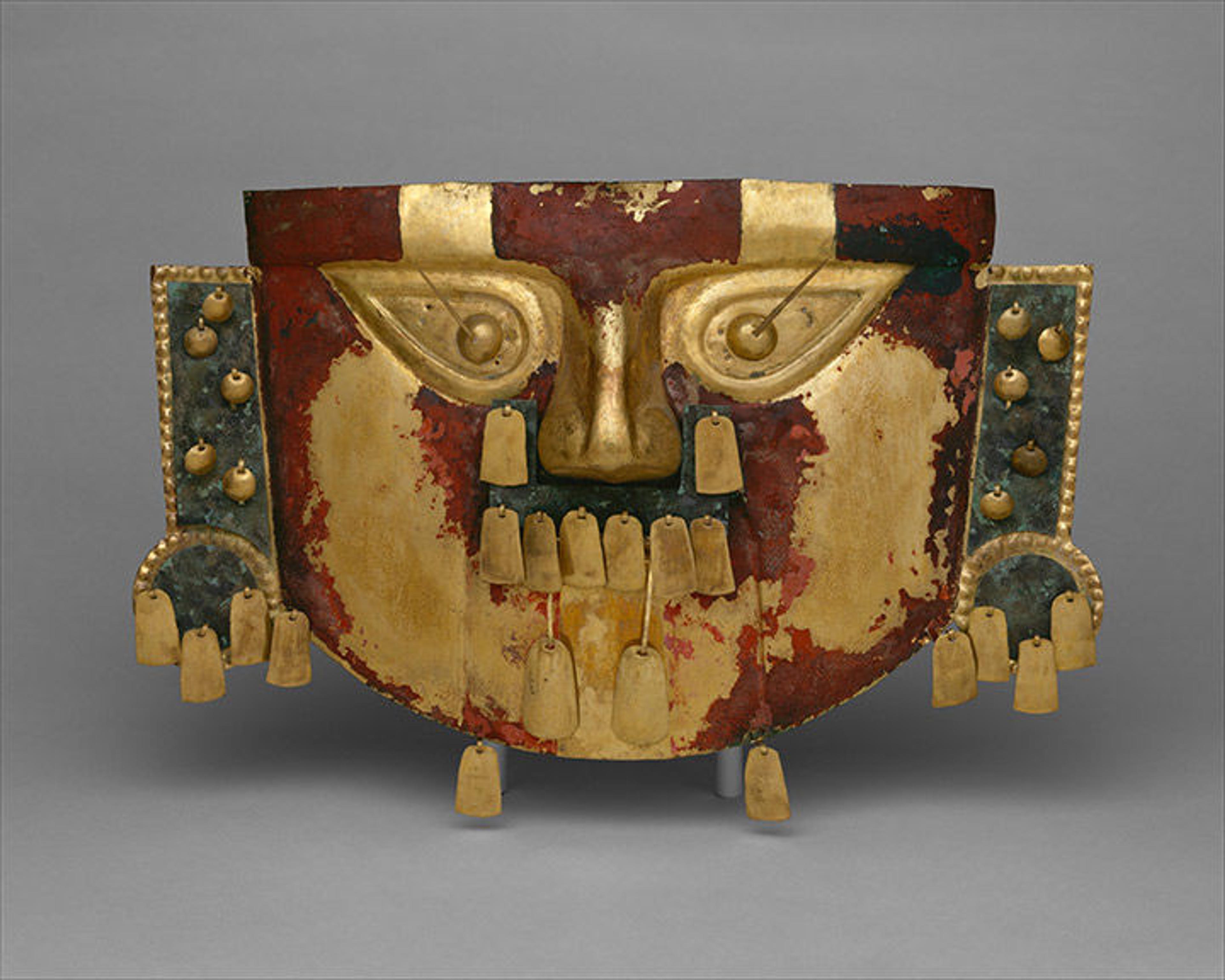 A photograph of a gold, red, and green funerary mask with prominent facial features.