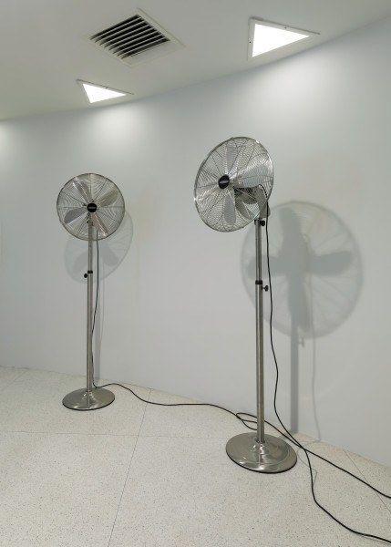 Two tall, motorized fans standing on the floor of an empty white room