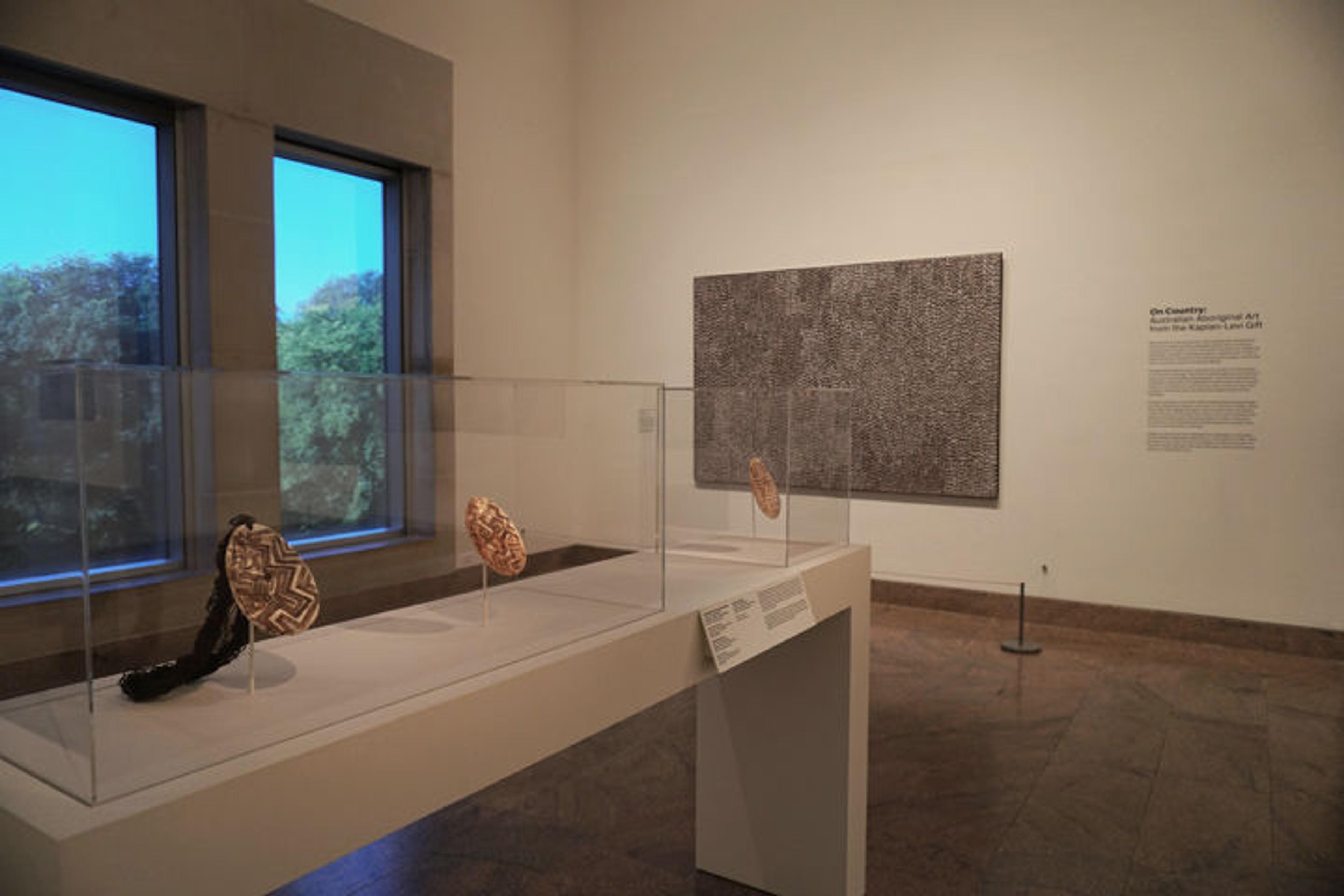 View of an exhibition gallery featuring one paintings and a collection of three Australian pearl-shell ornaments