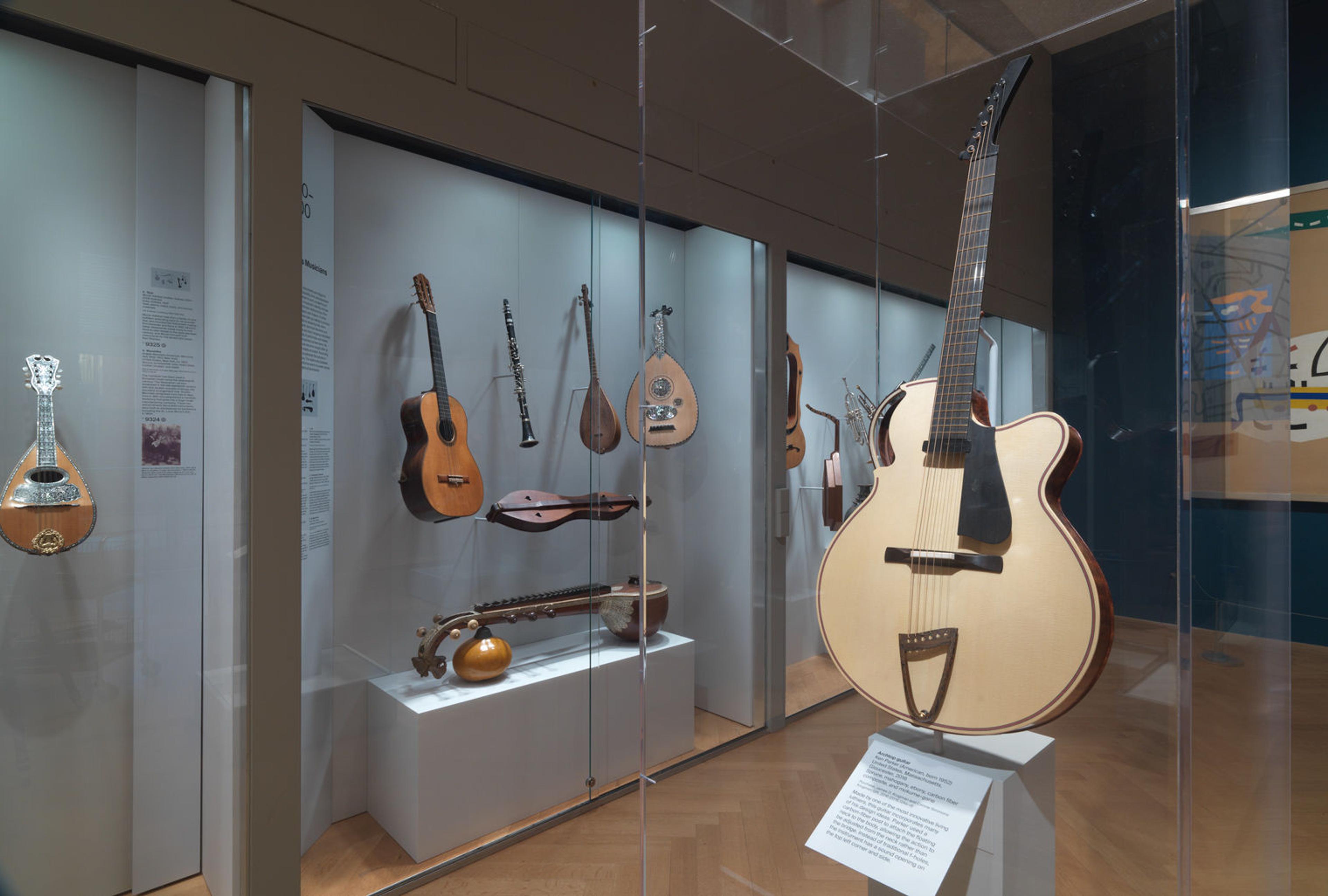 Picture of one of the musical instrument galleries at The Met, with several instruments such as guitars and mandolins in glass cases.