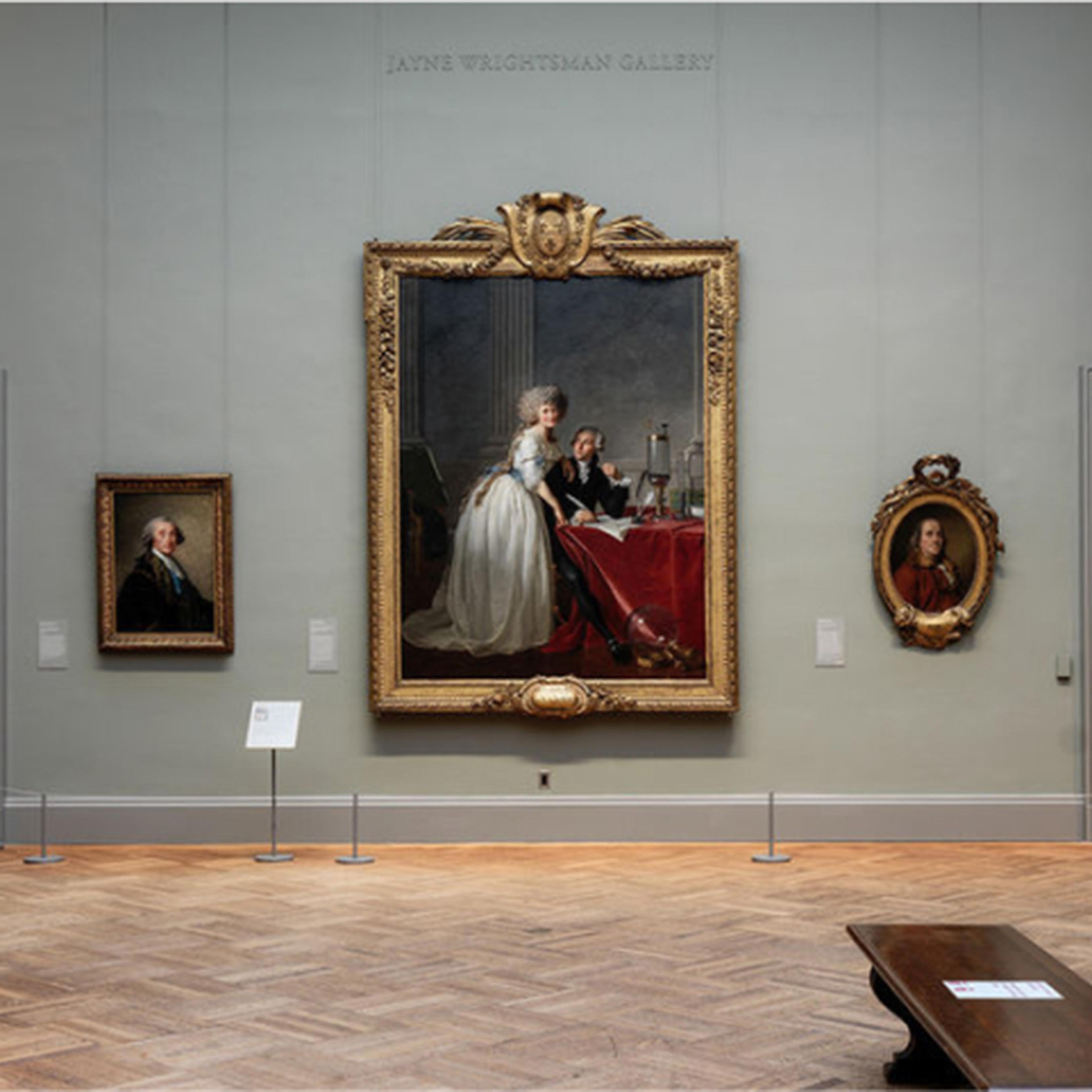 A spacious museum gallery showcasing various artworks, including paintings and a sculpture, with elegant wood flooring and neutral walls.