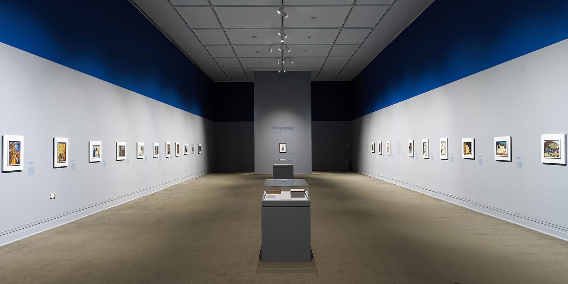 A photo of many paintings hanging along a gray gallery