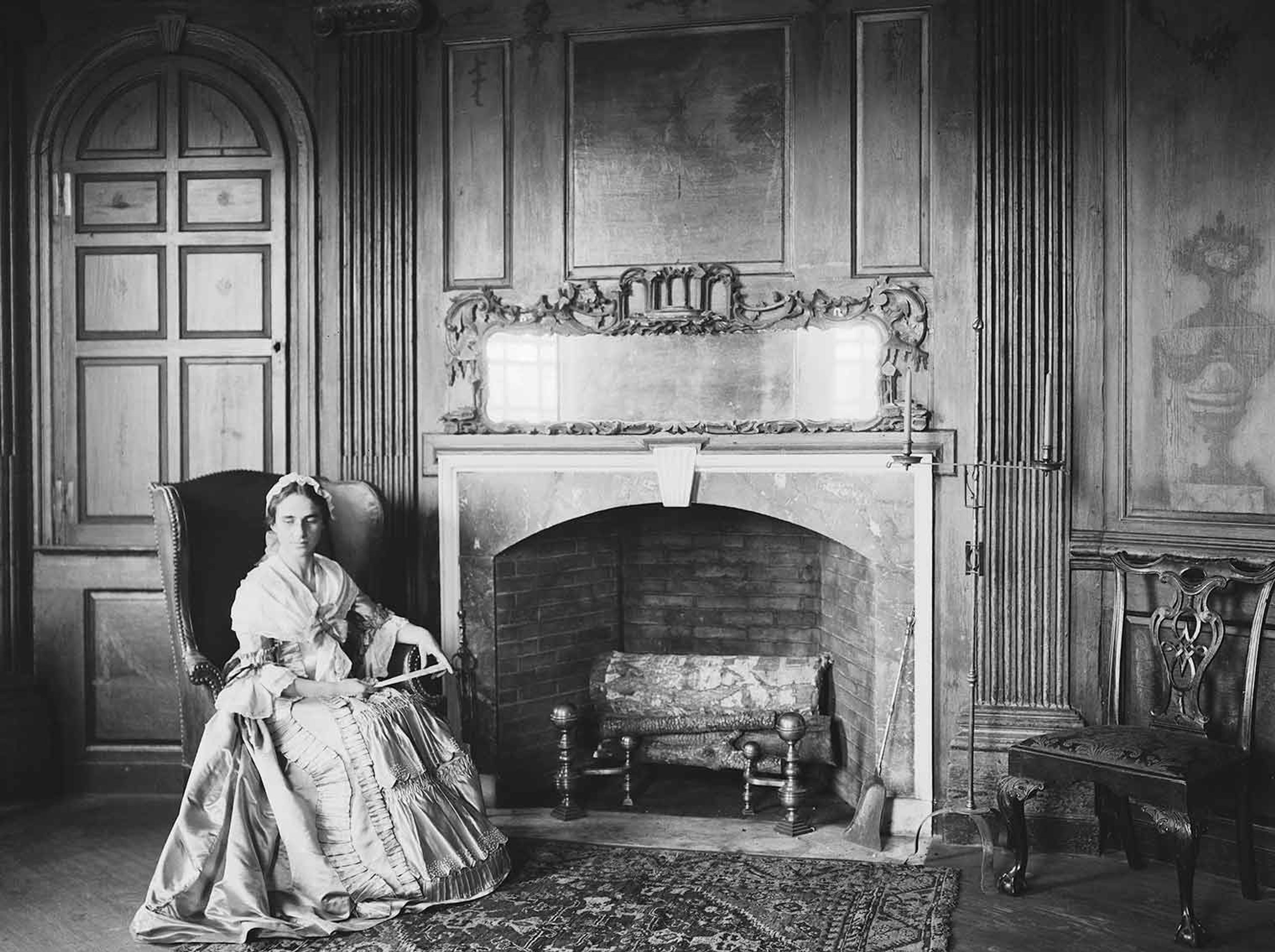 Black-and-white image of an actor in 18th-century period costume sitting in the Marmion Room