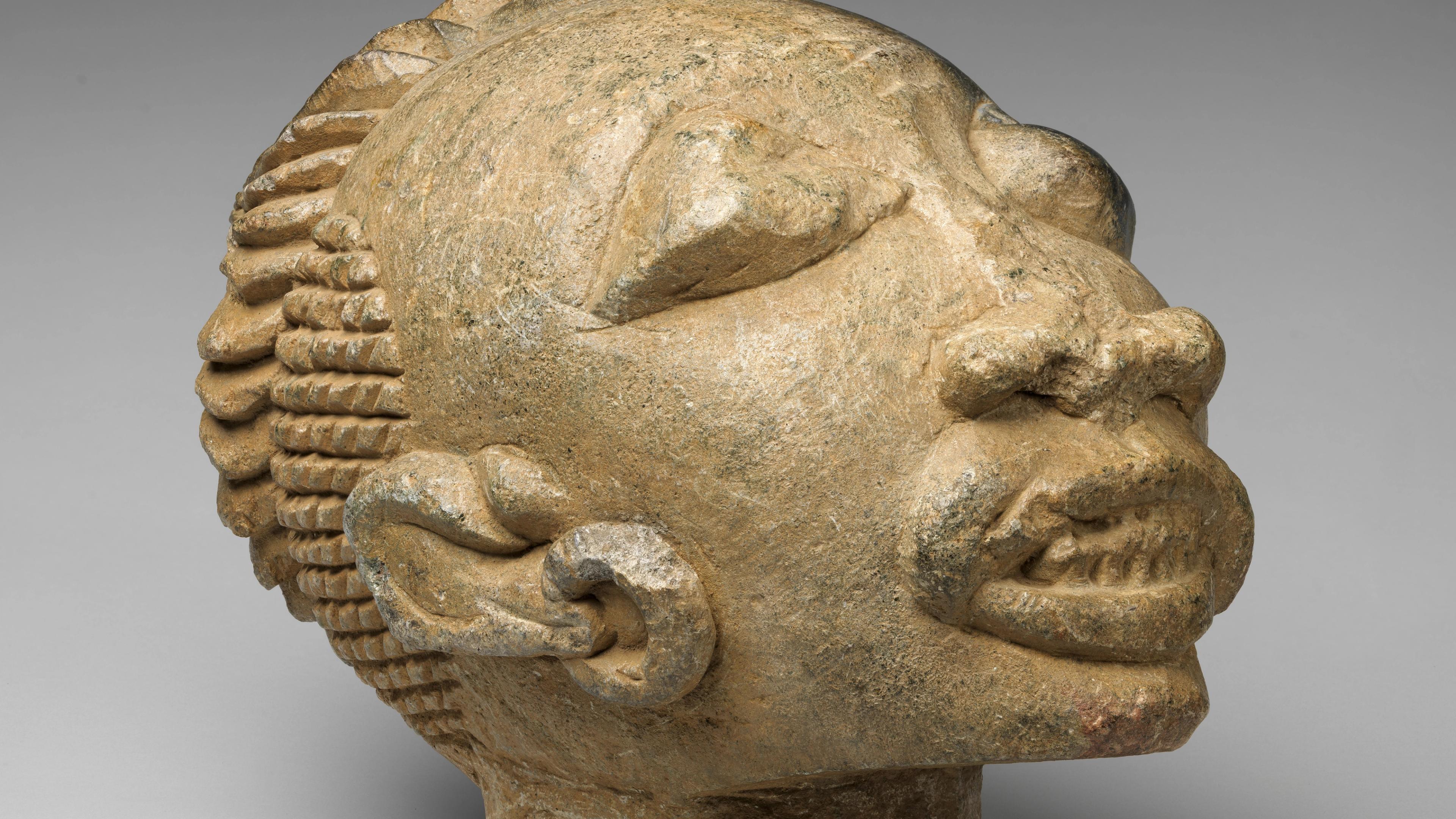 Large stone head with bold features, filed teeth, and an elaborate cap or coiffure signifying a high-ranking individual.