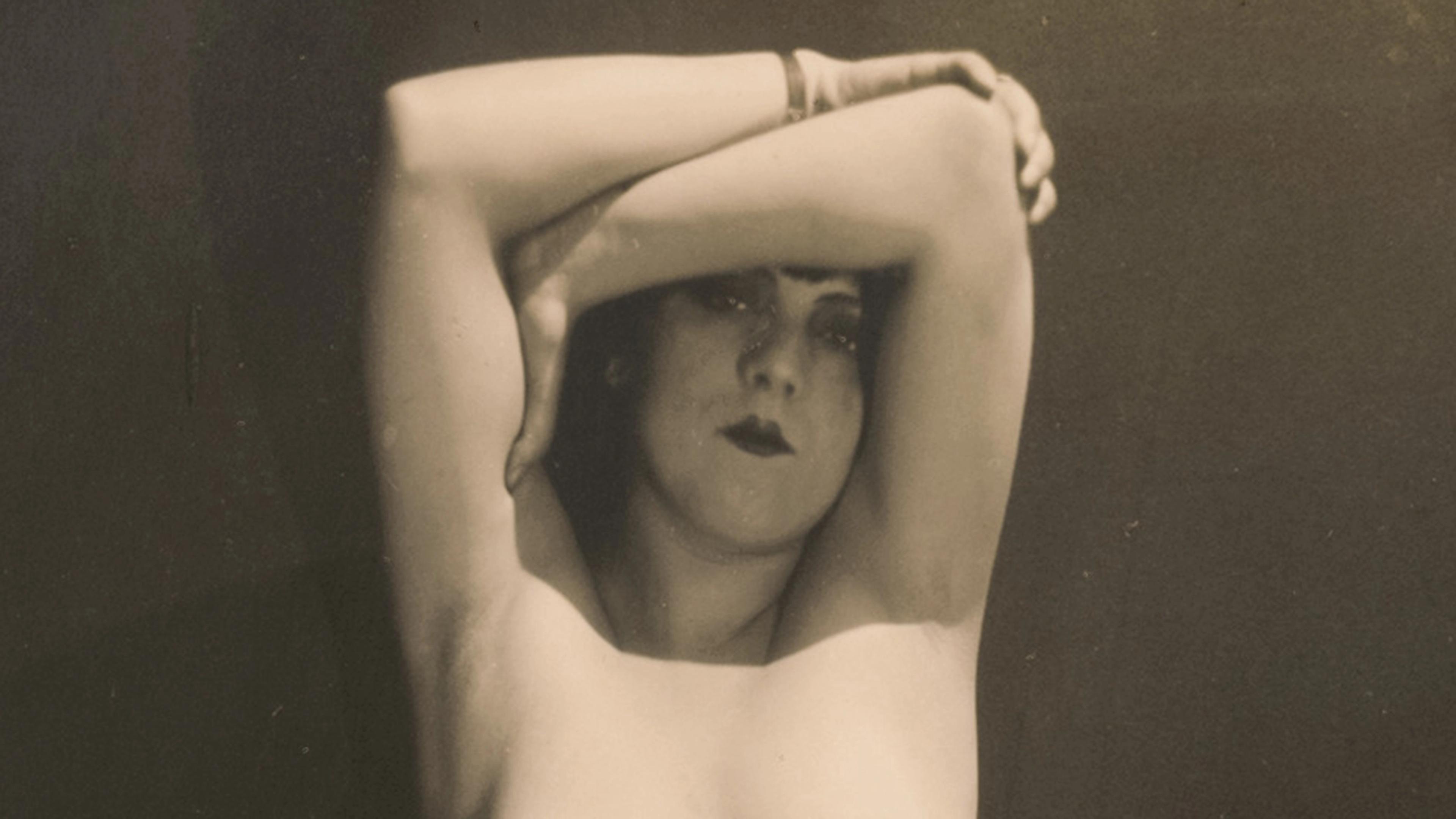 Black-and-white photograph of a woman with her arms overhead framing her face.