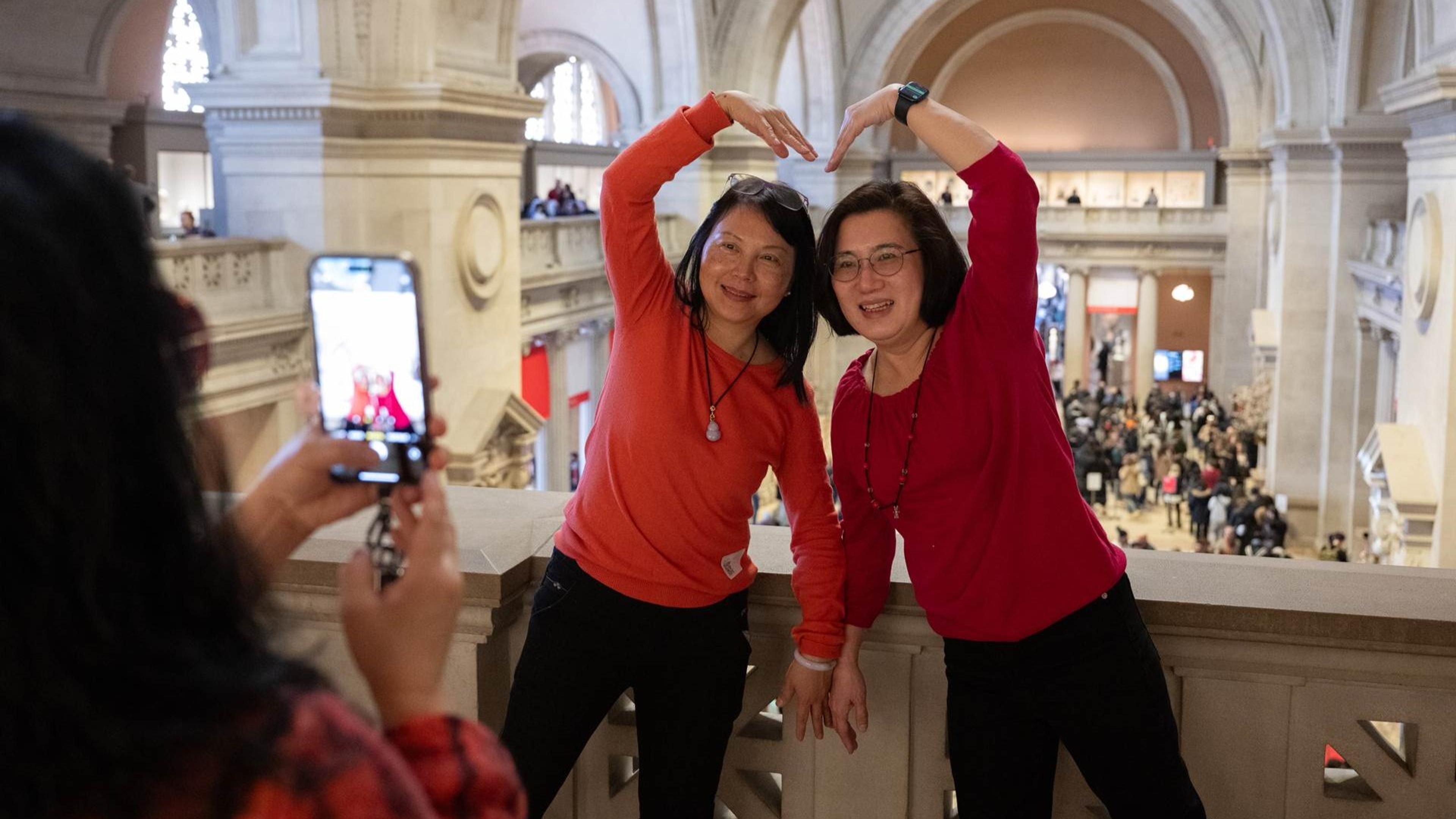 Two people make a heart shape with their arms while another takes their photo