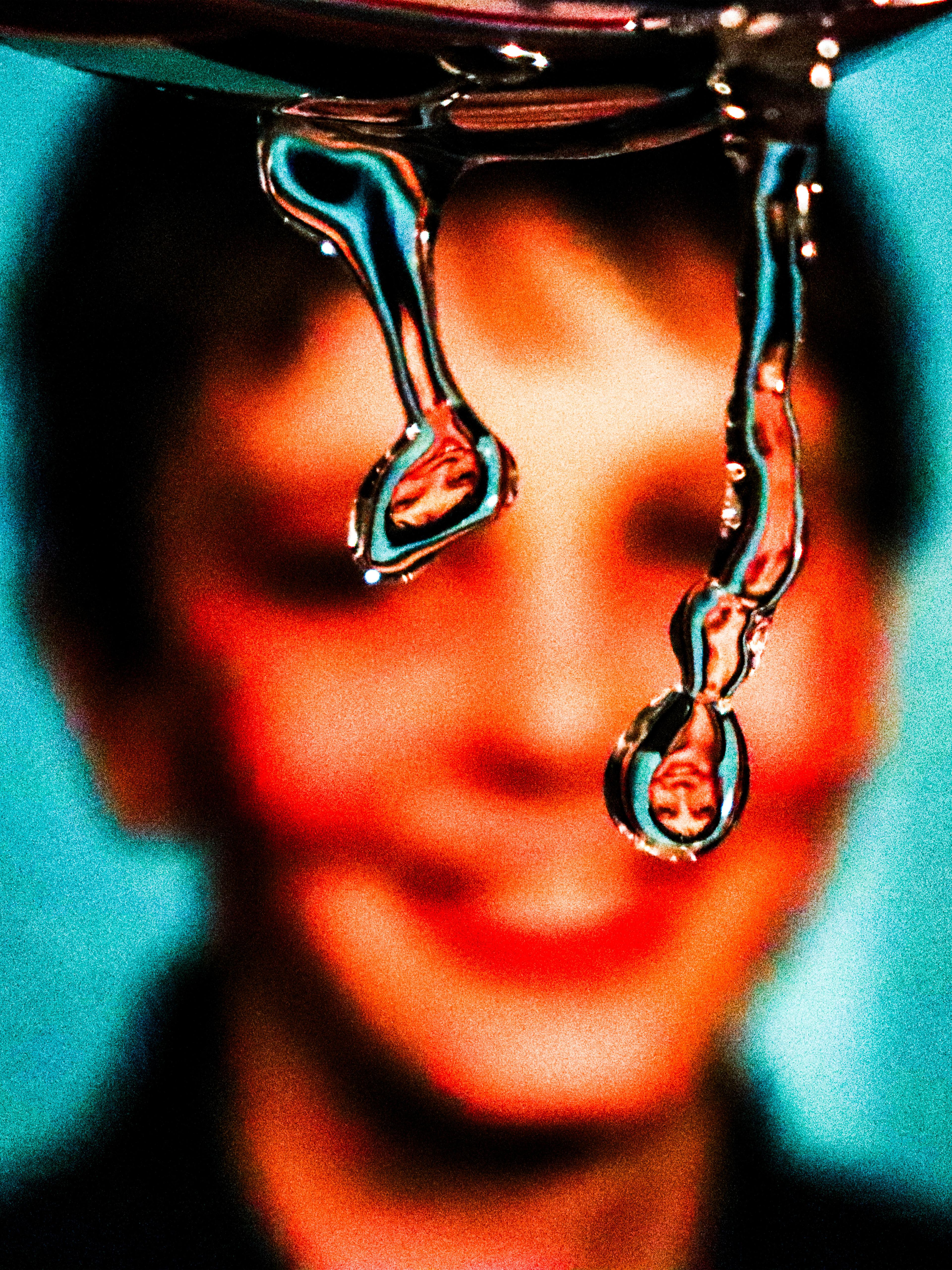 Close-up of two liquid-like droplets reflecting an upside down image of a smiling face in the background.