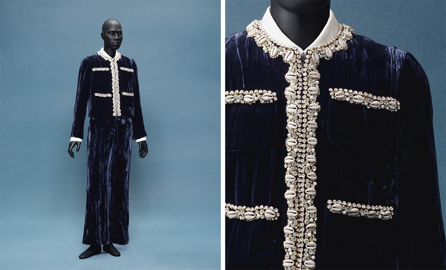 A mannequin wearing an elegant, navy velvet suit embellished with pearls and shells on the collar and pockets. The background is a muted blue.
