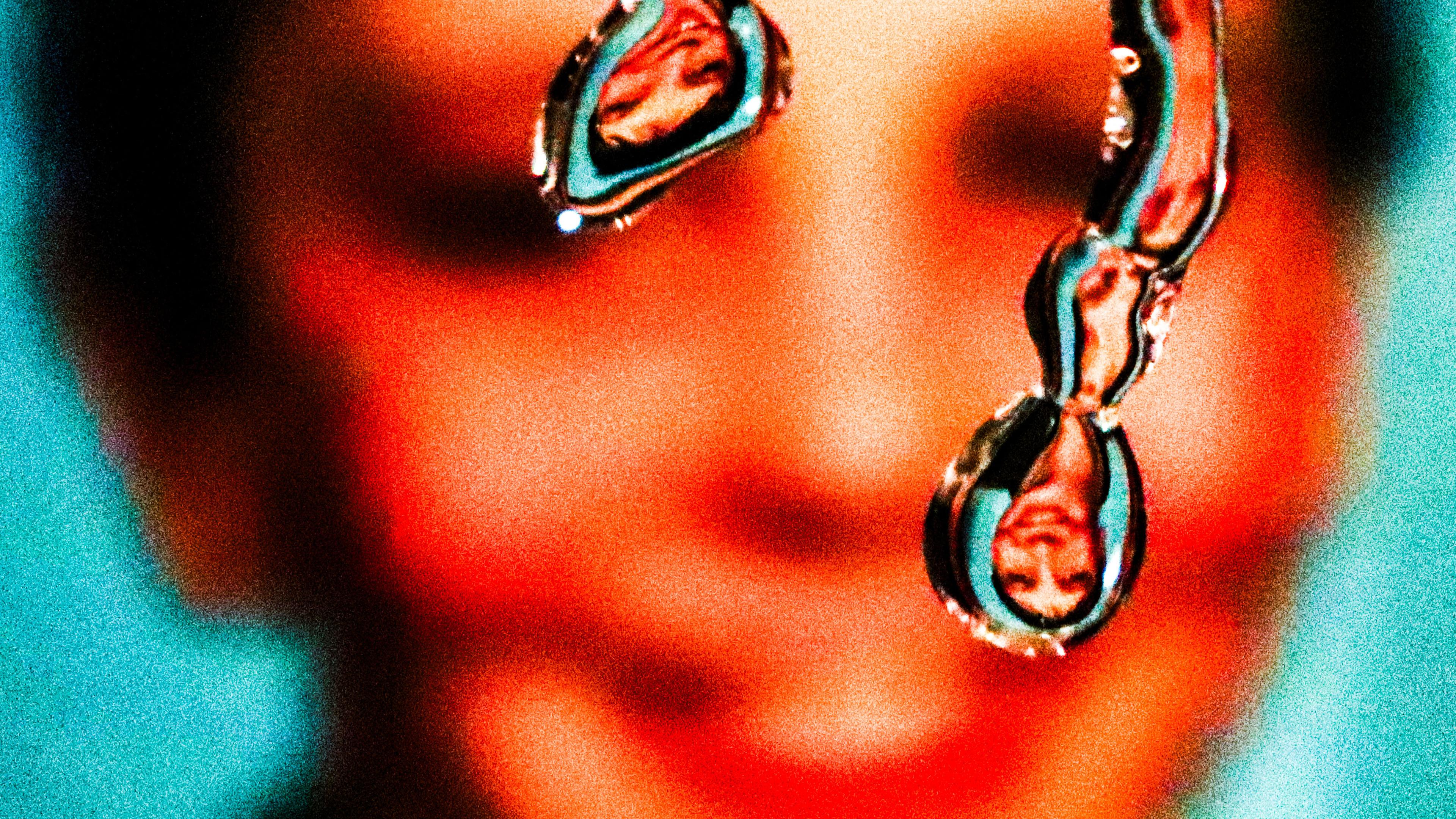 Close-up of two liquid-like droplets reflecting an upside down image of a smiling face in the background.