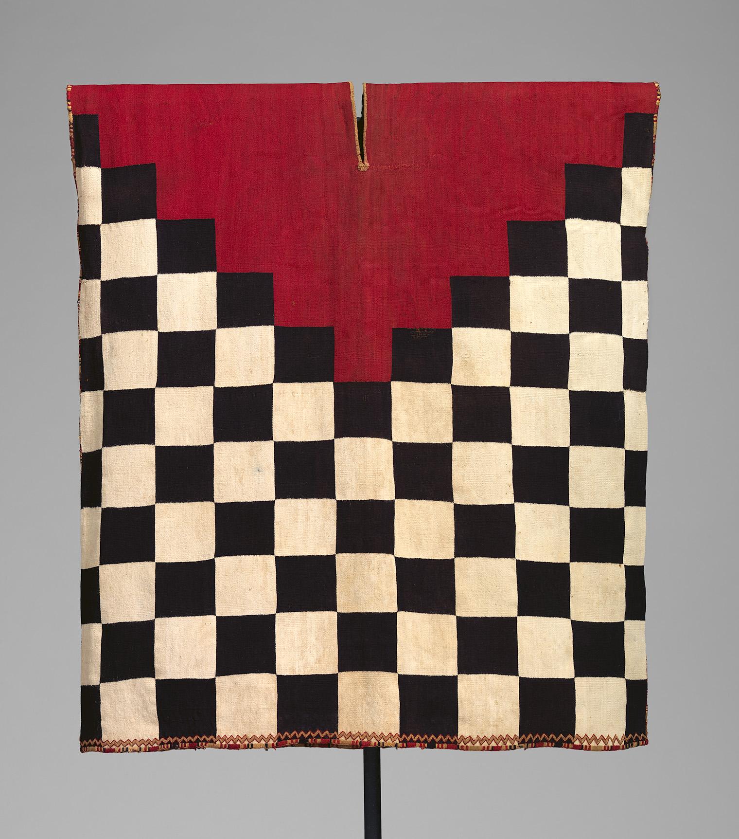 A red-and-black checkerboard textile hangs against gray, with cream squares, a notched red top, and a dark lower rod; bold, graphic tone.