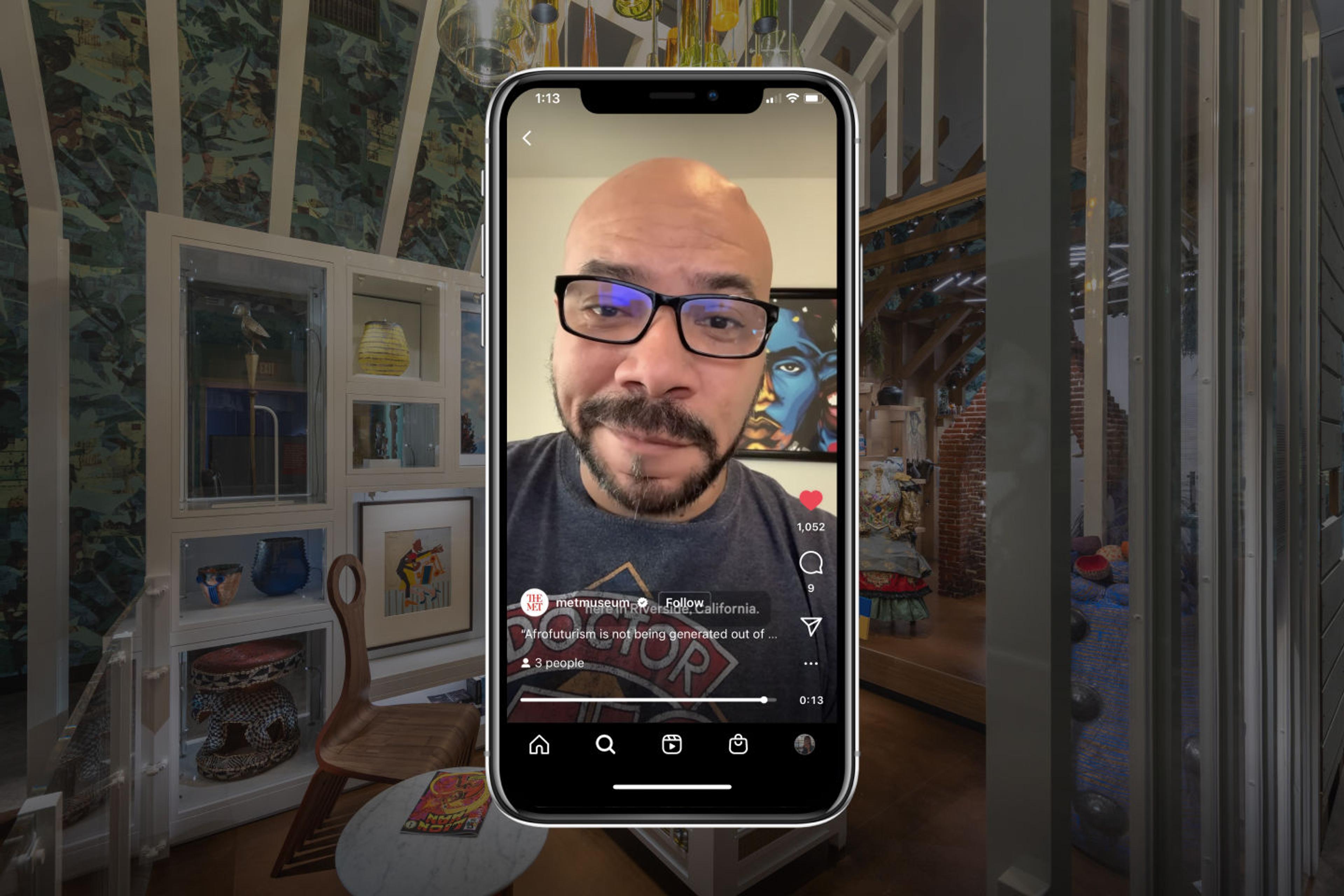 The bestselling author and illustrator John Jennings is visible on an iPhone before a backdrop of the Afrofuturist period room currently on view at The Met.