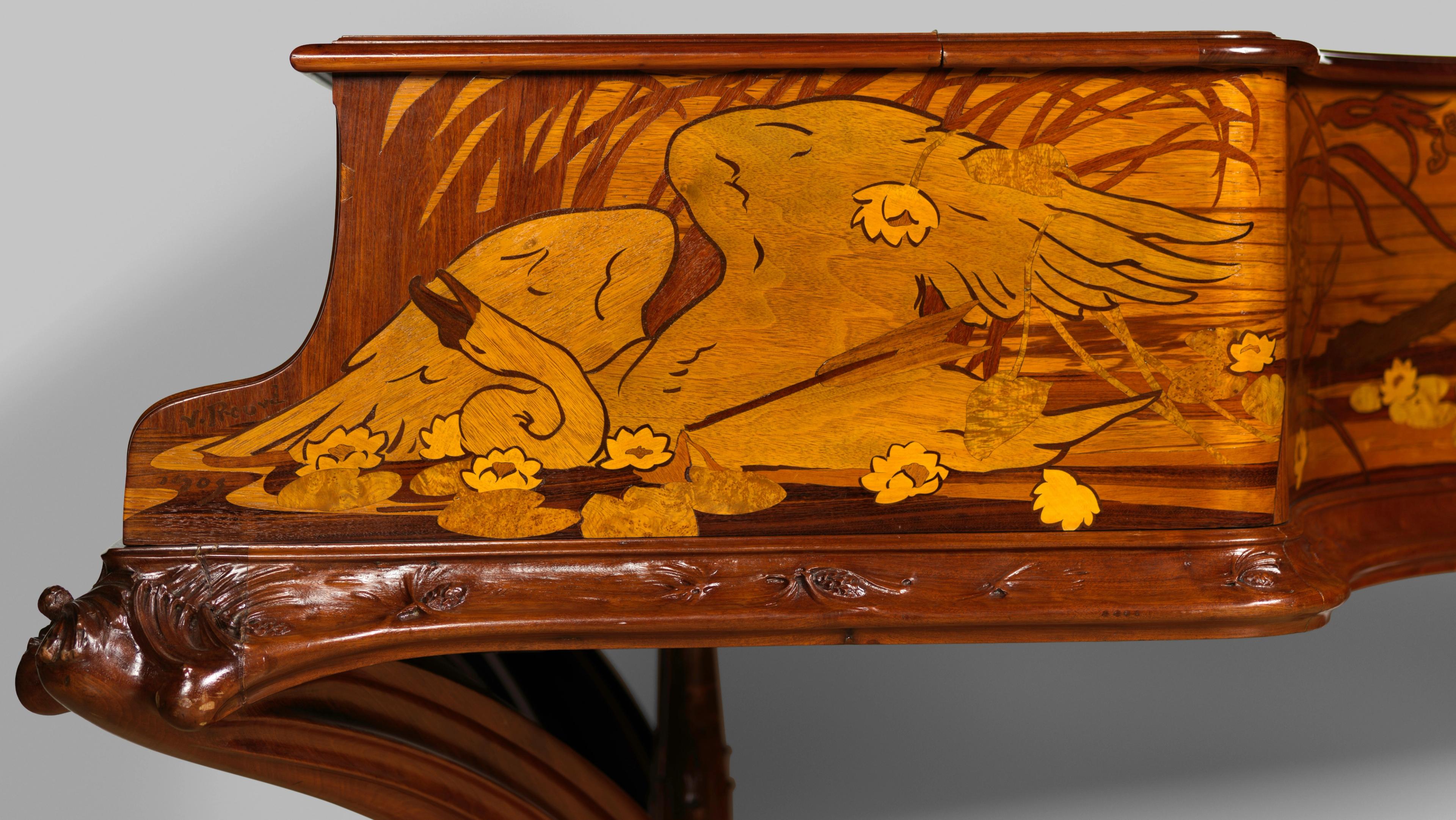 An engraving of a dying swan on the side of a brown wooden piano.