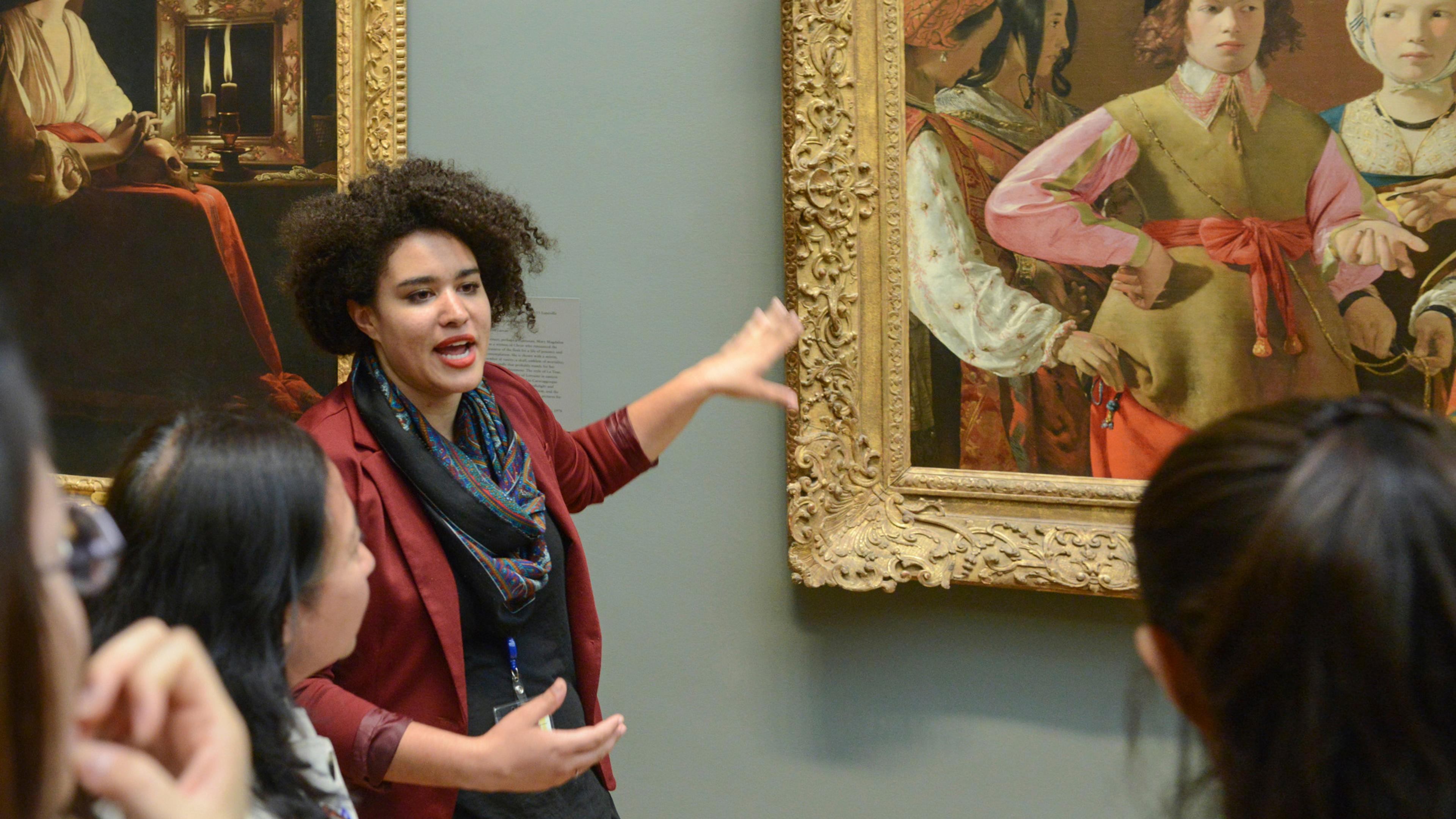 Tour Guide pointing to a painting and explaining the context to a group of visitors.