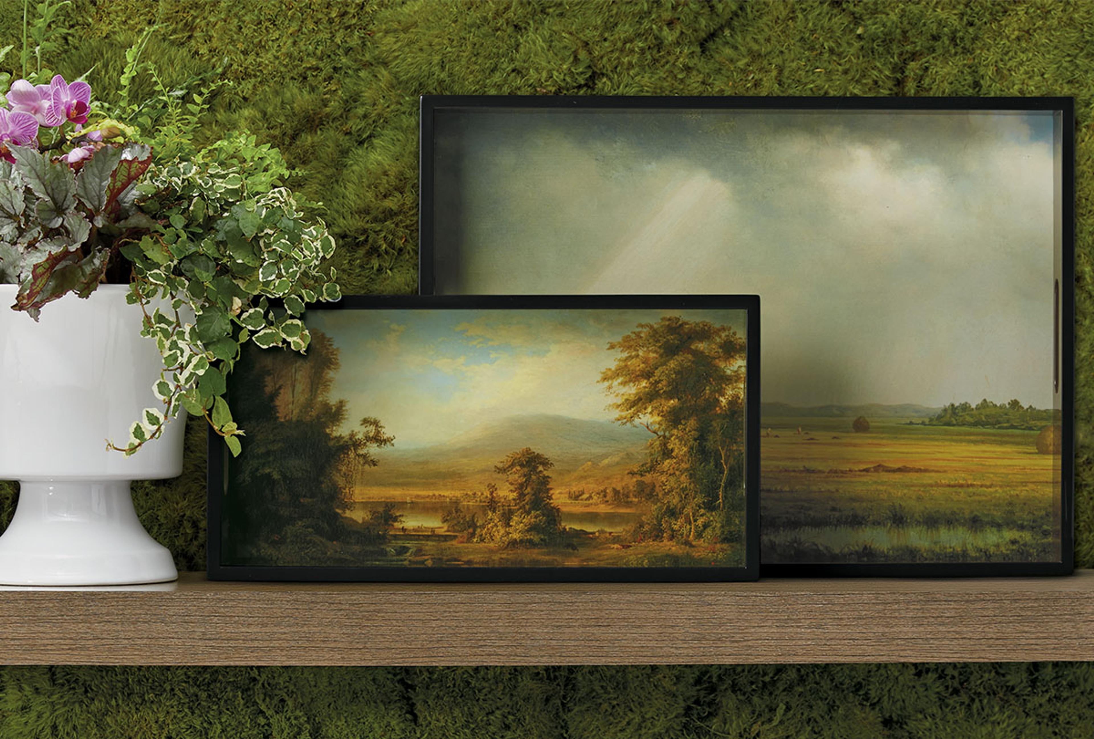 Two framed landscapes sit on a wooden shelf next to a floral arrangement.
