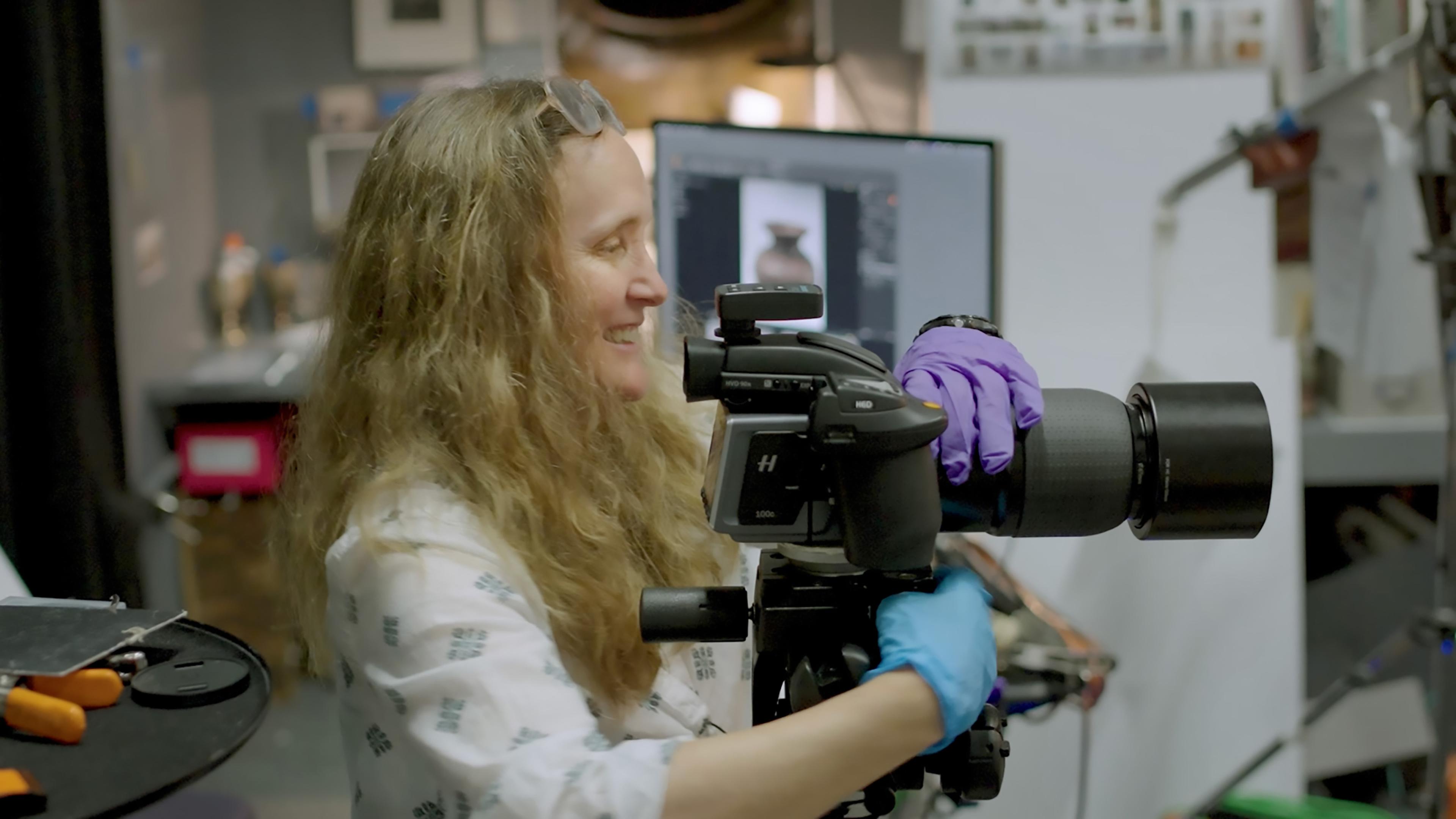 Photographer Eileen Travell smiling and adjusting a camera on a tripod.