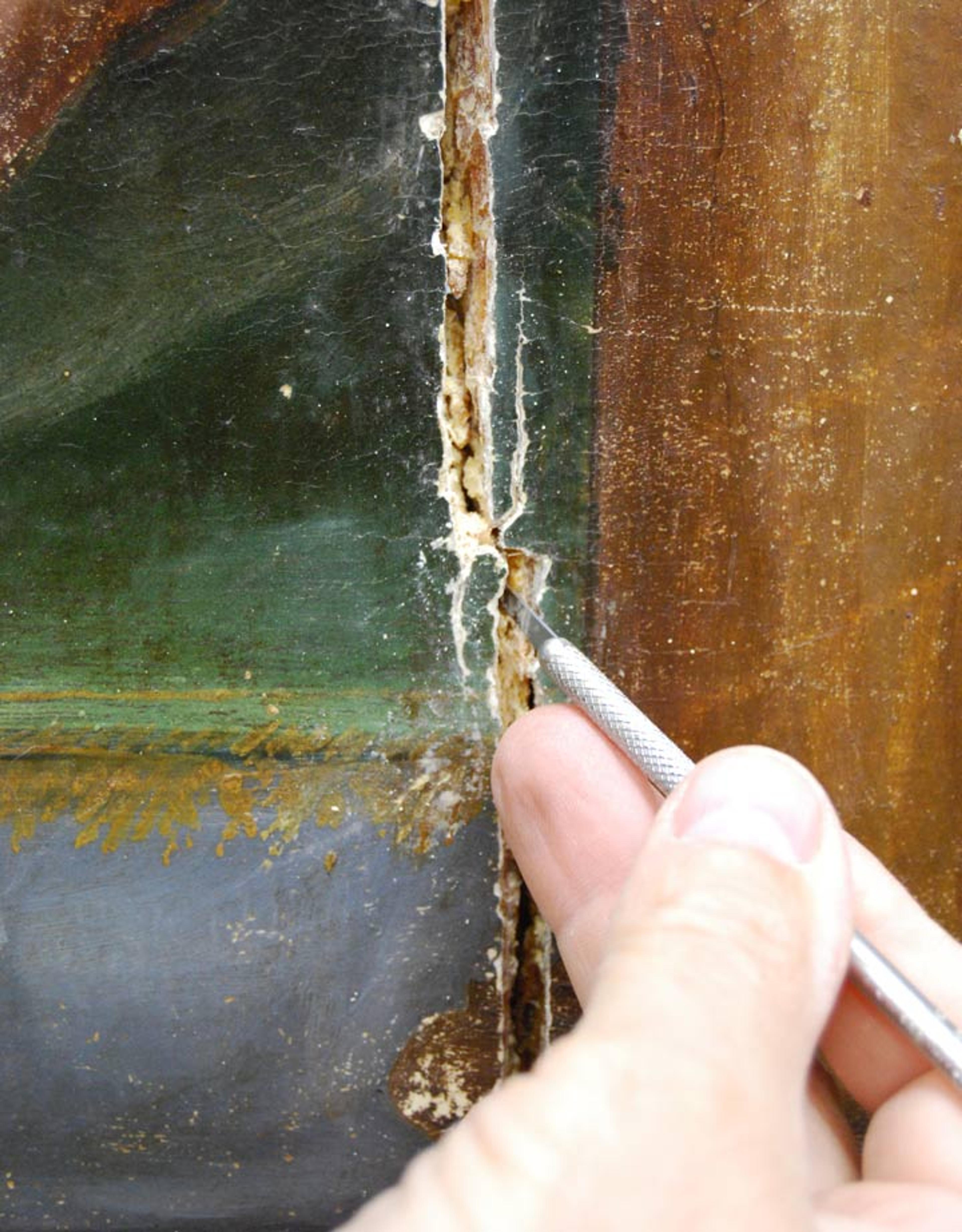 Hand inserting a tool into a crack in the painting