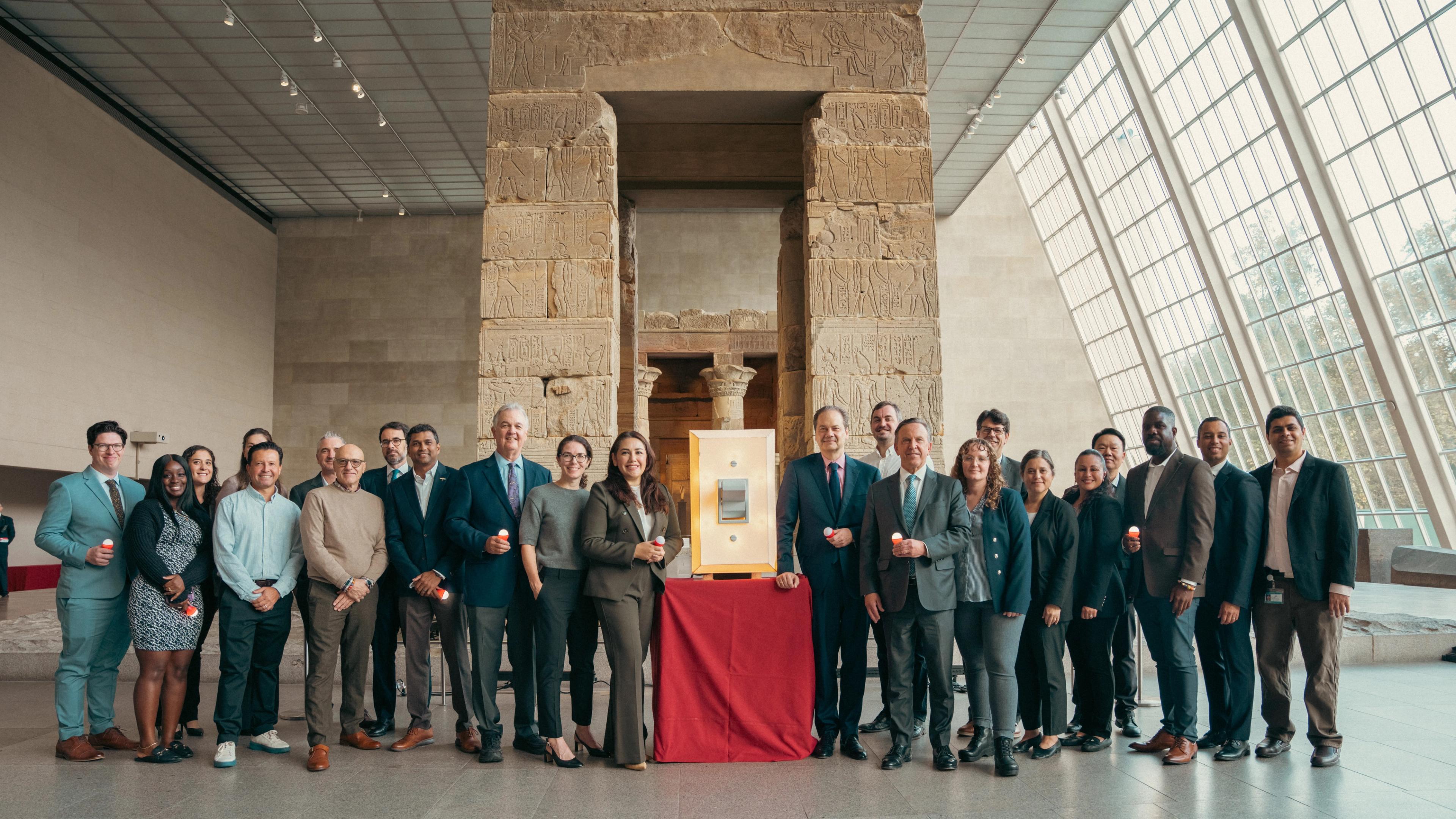 A group of people smiling standing in front of an Egyptian Temple with a light switch at the center
