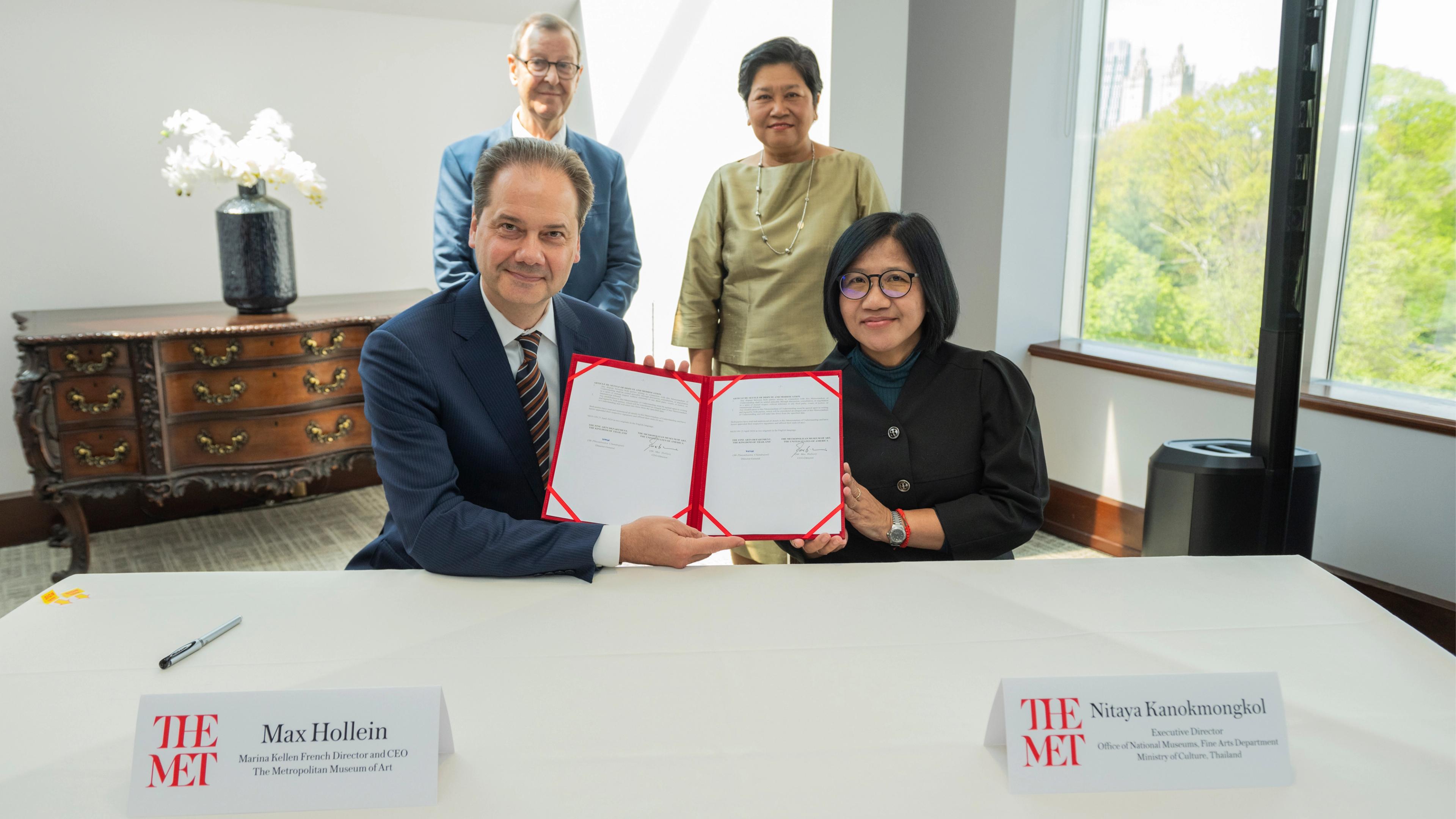 Max Hollein and Nitiya Kanokmongkol sign a partnership agreement, with four individuals standing behind them in a bright conference room.