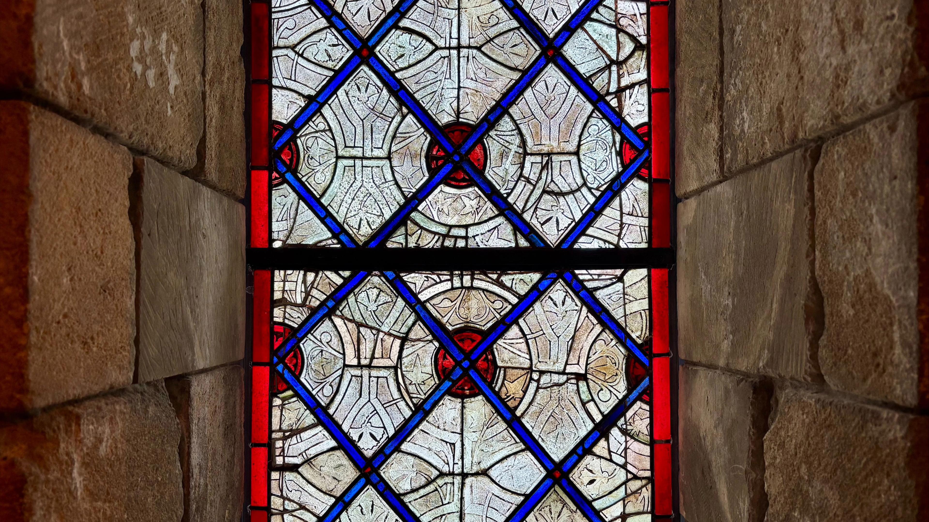 A blue and red stained-glass window nestled between rectangular stones.