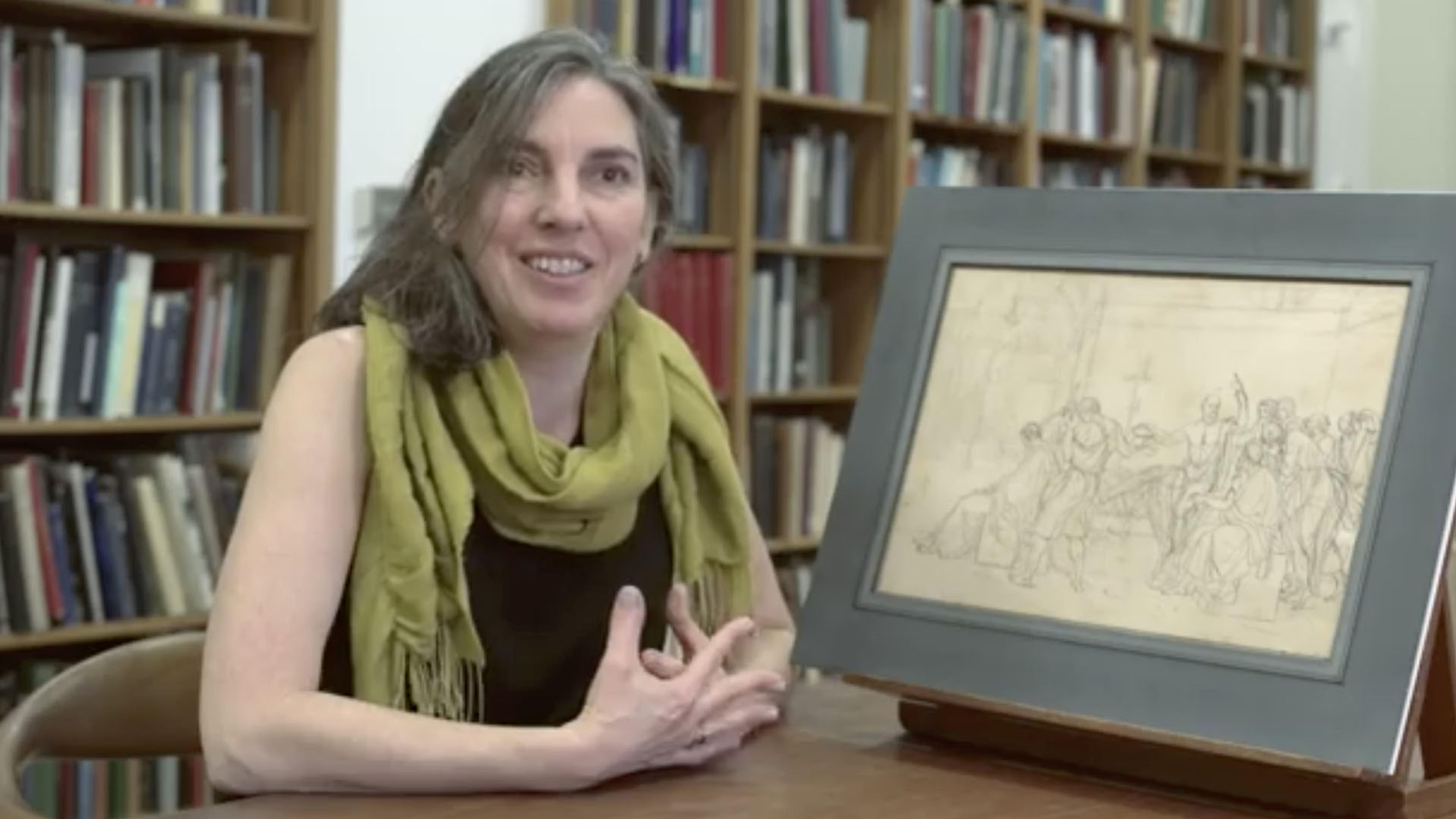 Woman in a green scarf discussing a drawing that sits on a table in a library