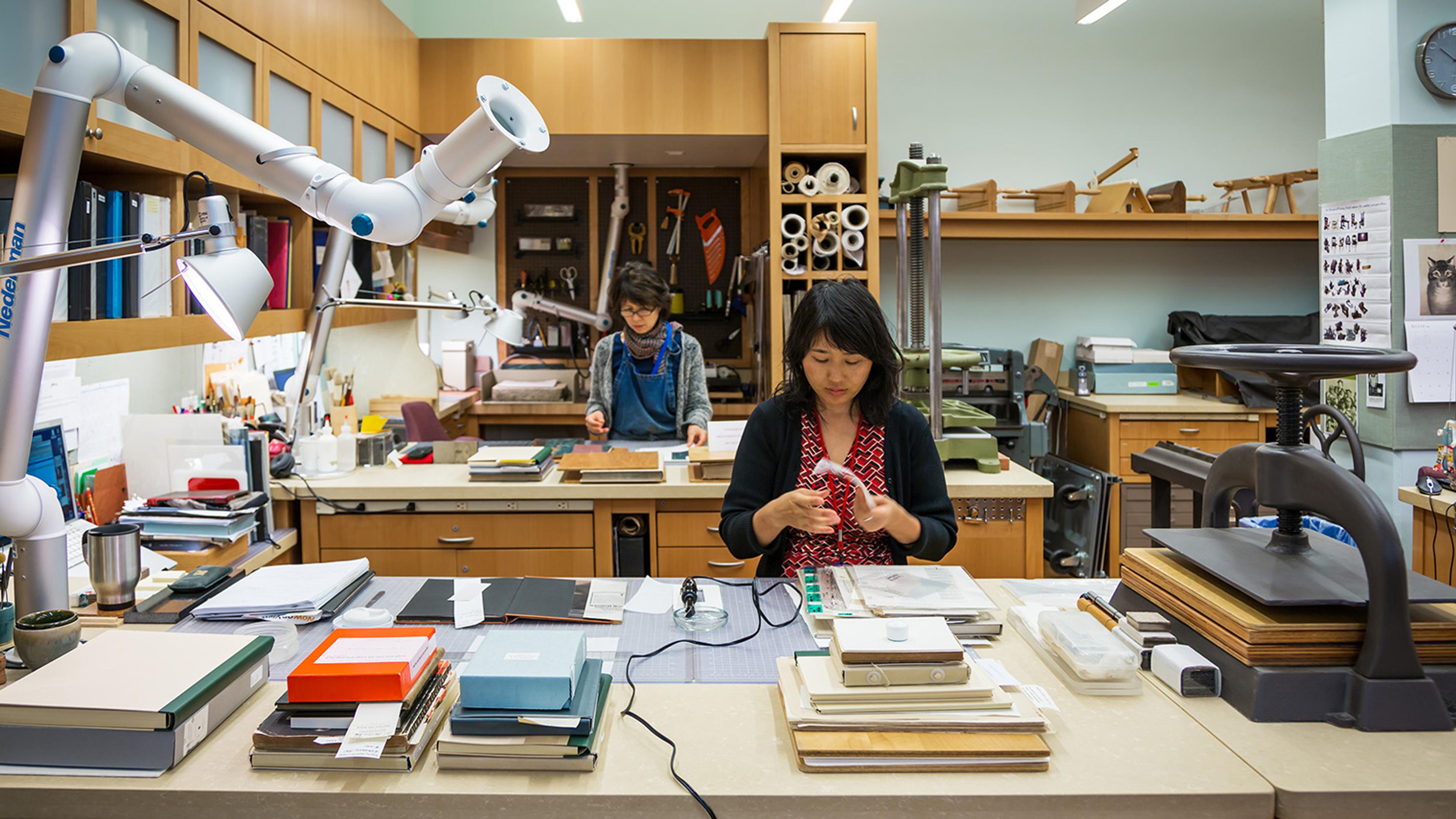 Two conservators working in a studio filled with various tools and books.