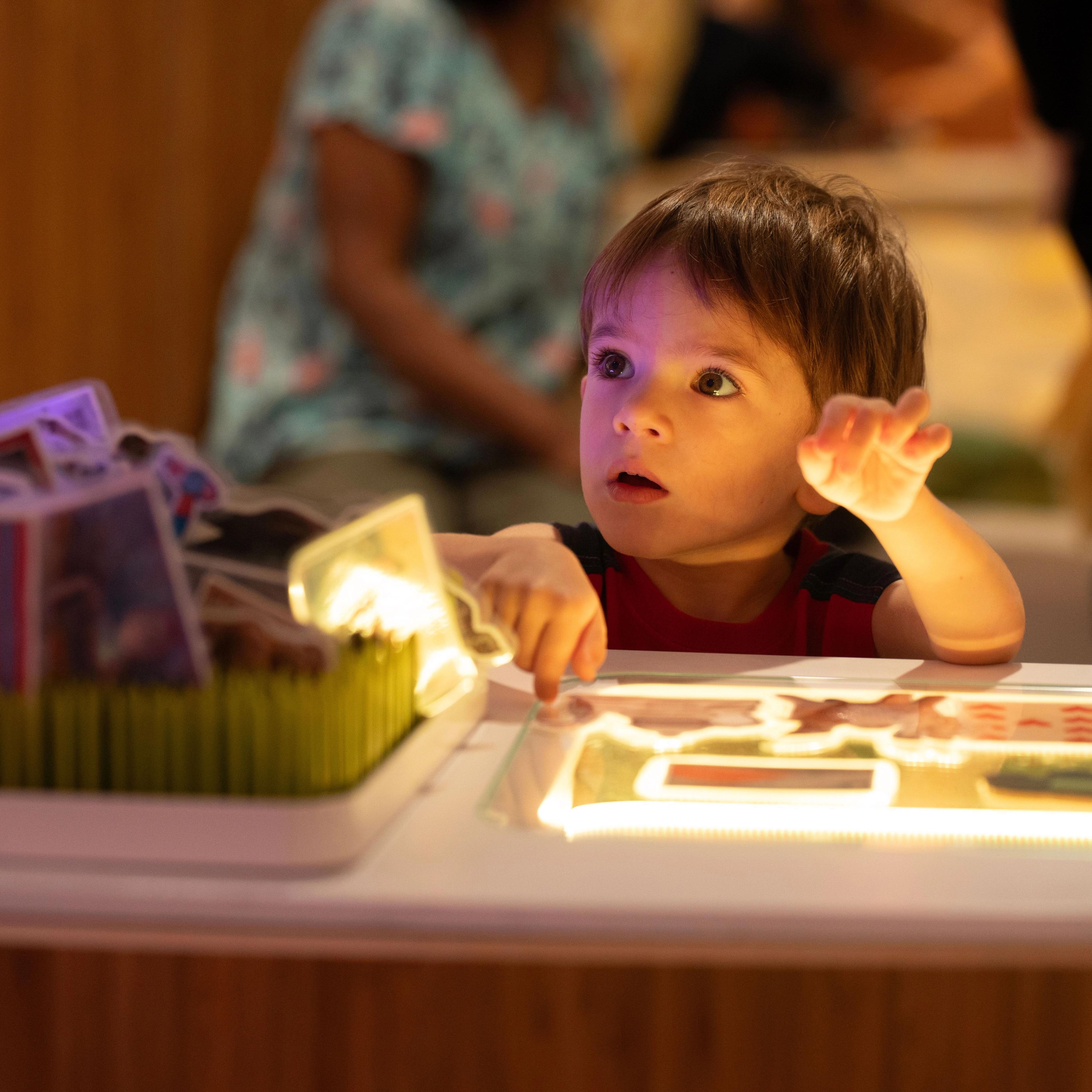 Young child at a low table with lights and cards, looks up.
