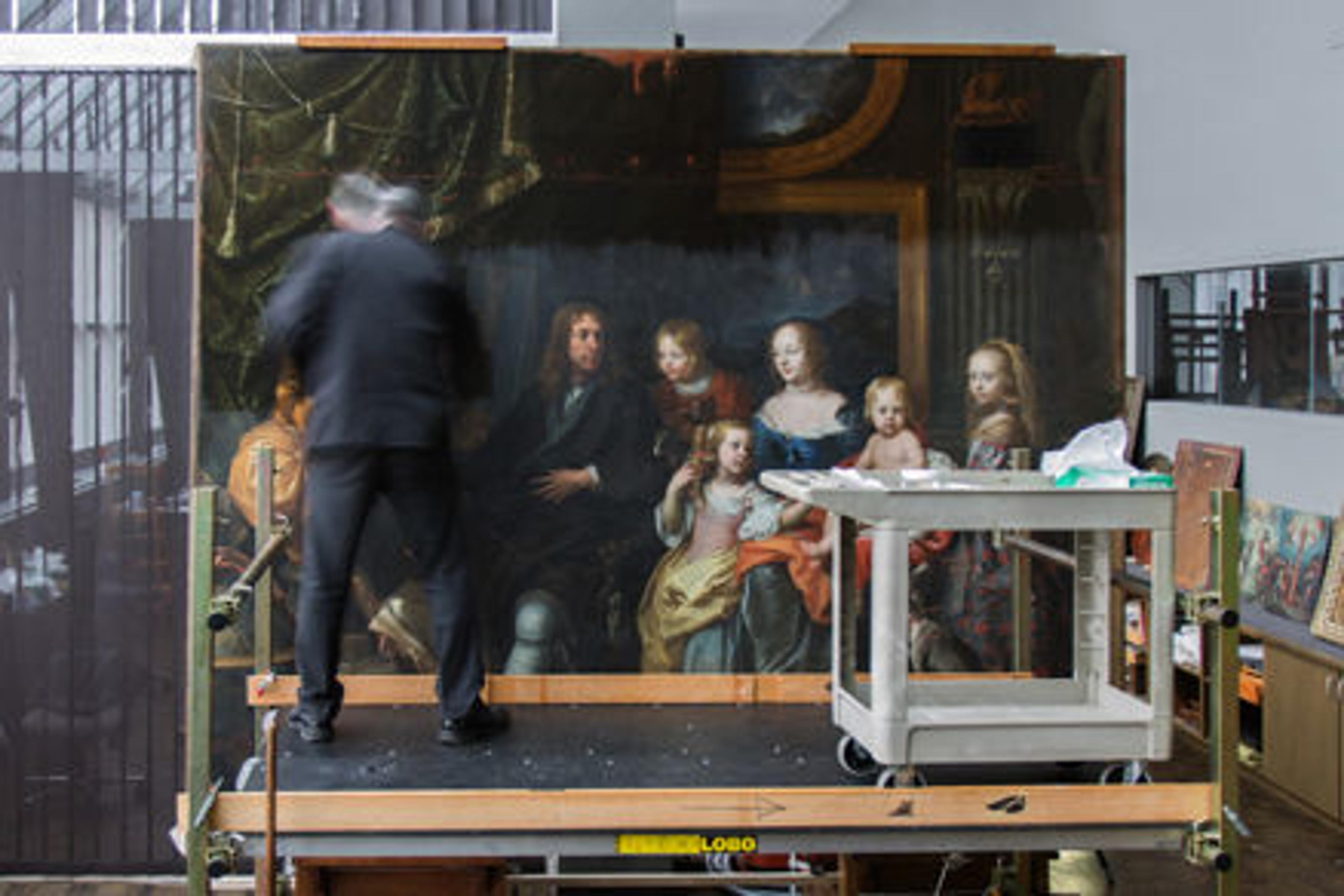 Blurry photo of a conservator standing in front of a painting, surrounded by conservation tools