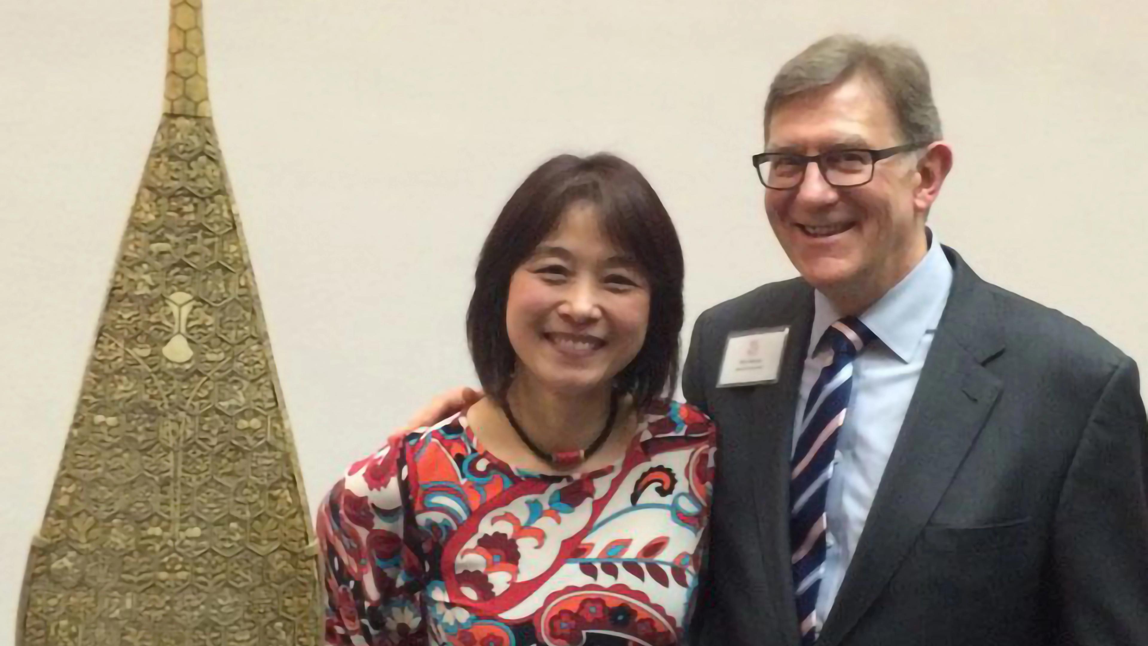 Wu Man and Ken Moore stand smiling next to an ornate pipa elevated on a pedestal.