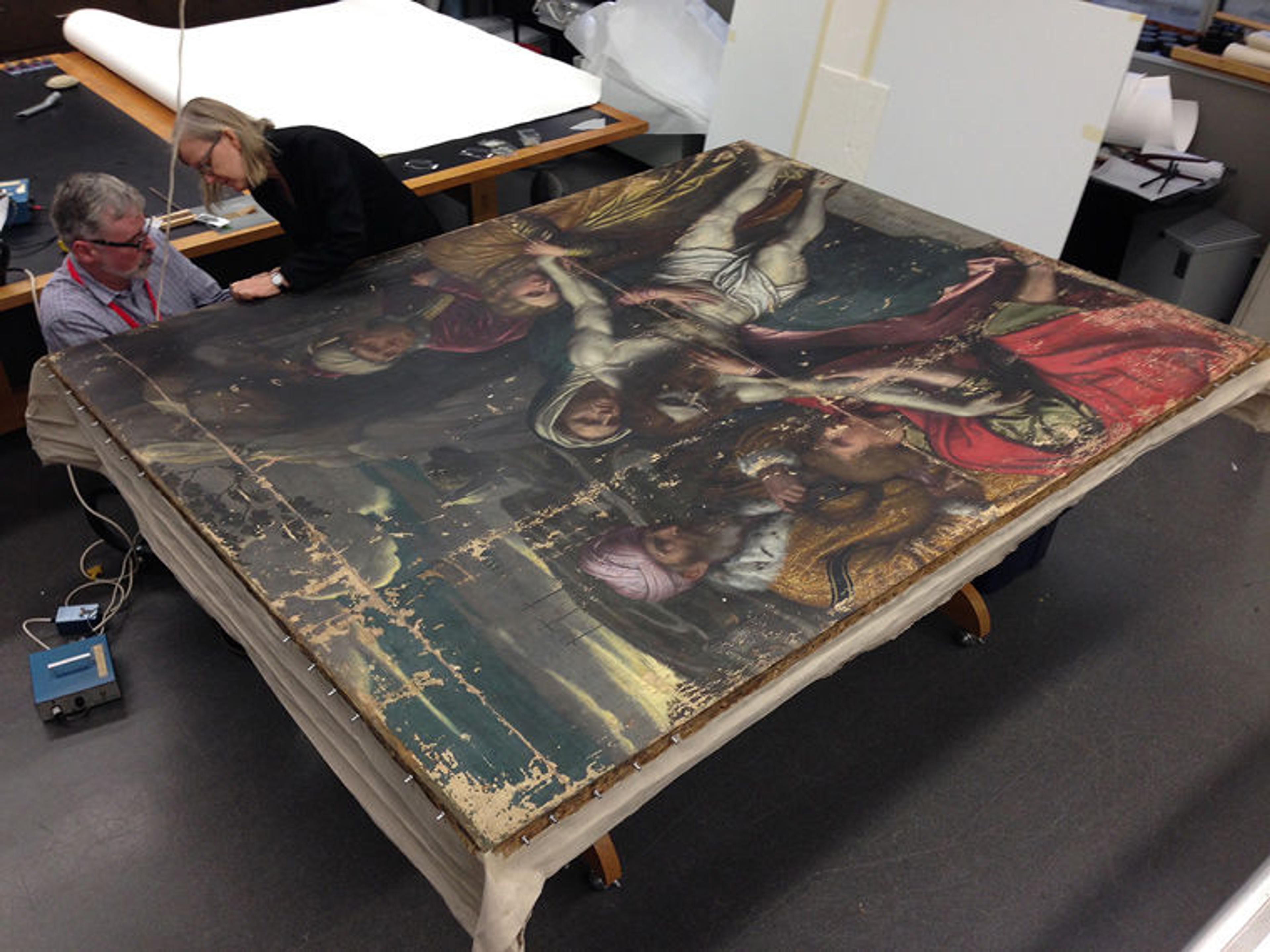 Two conservators put a sixteenth-century painting on a stretcher during conservation treatment