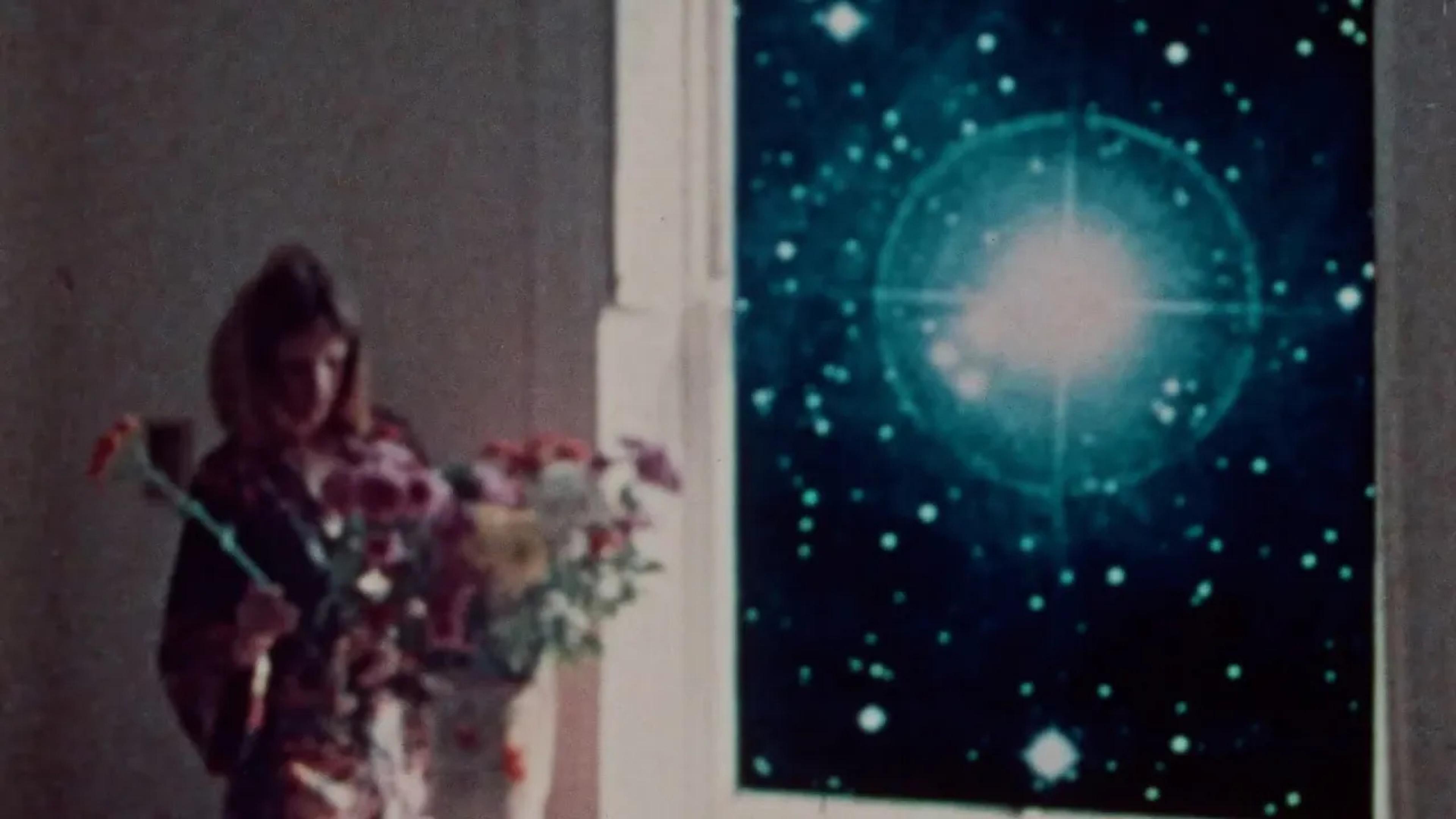 A woman arranges flowers in a dim room, while a glowing starry nebula is visible through a nearby window.